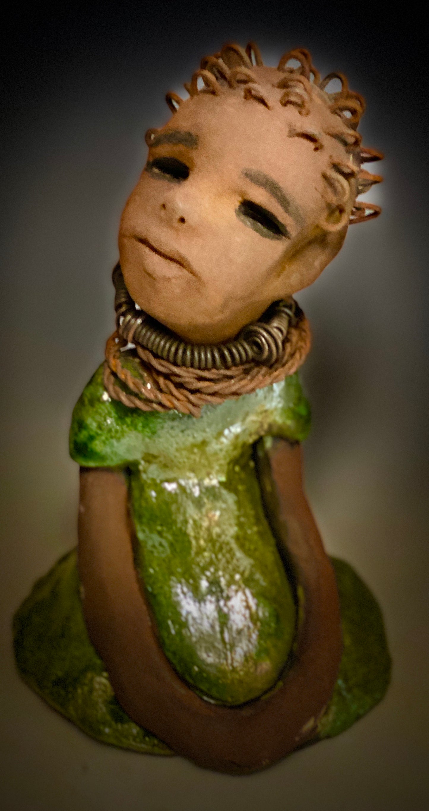 Meet Nura! Nura stands 7.5" x 5" x 5" and weighs 1.06 lbs. She has a lovely honey brown complexion with reddish brown lips. She has a wire braided hairstyle. Nura has a colorful metallic green antique copper glazed dress. She wears spiral wire necklaces With her eyes wide opened, Nura has hopes of finding her way into your home.
