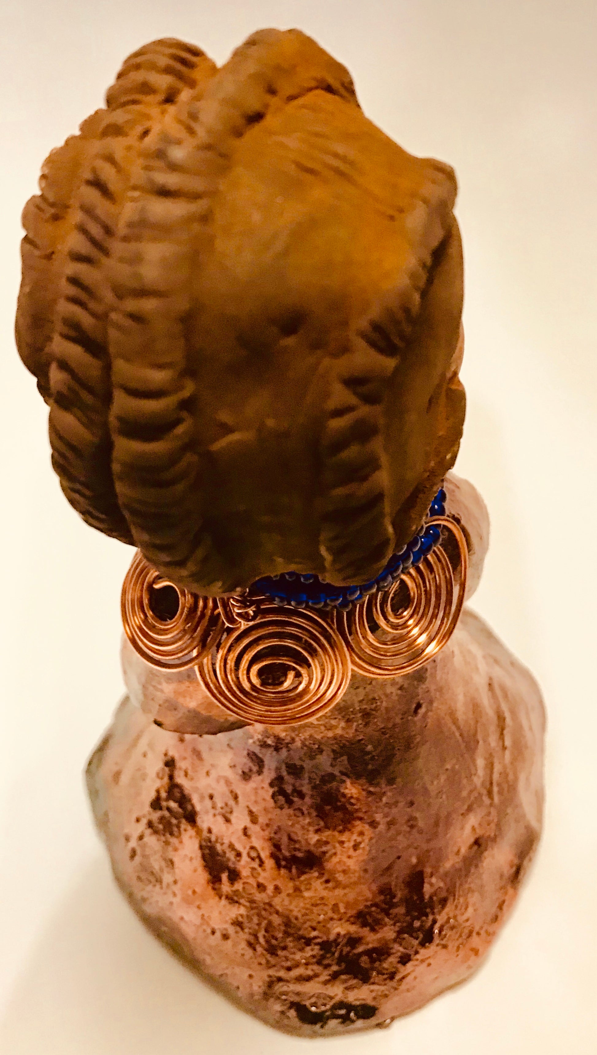 Ife stands 7.5" x 4" x 5" and weighs 1.02  lbs. She has a lovely honey brown complexion with reddish brown lips. She has a short braided hairstyle.      Ife has a colorful metallic antique copper glazed dress.     She wears spiral copper wire necklaces on top of an aqua blue beaded collar.     Ife long loving arms rest at her side.     With accent blue eye shadow and eyes wide opened, Ife has hopes of finding a new home.