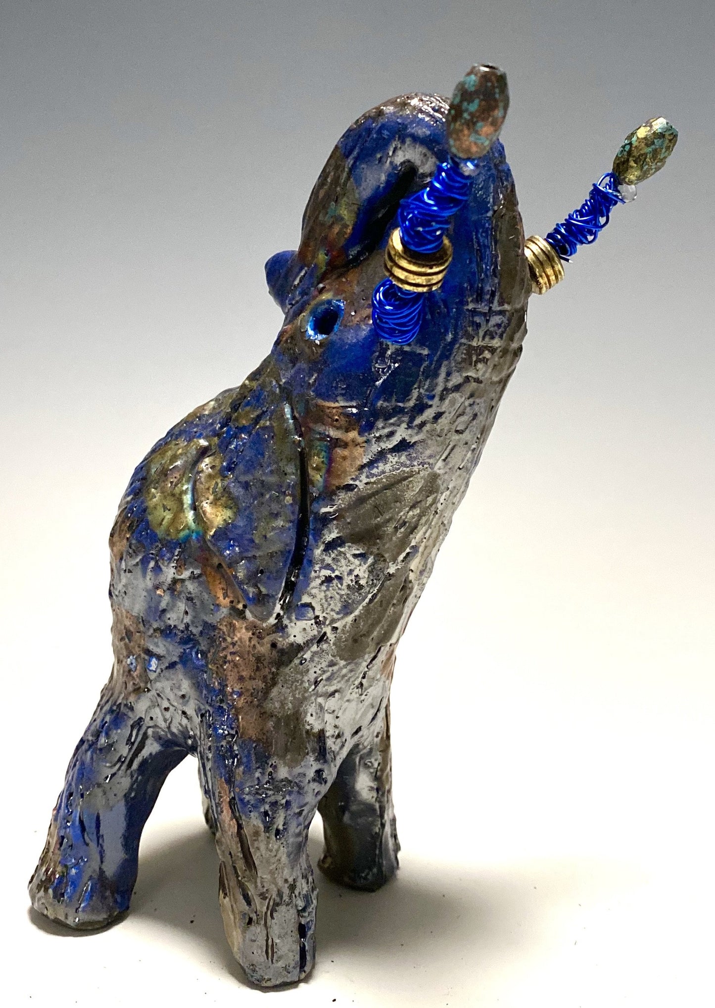 Raku Elephant Have you HERD!!!!!! Just one of these lovely Raku Fired Elephant will make an excellent gift for your friend, sorority or for your home’ special place centerpiece. 7" x 4" x 4" 14 ozs. Blue wire beaded blue tusk Beautiful metallic raku colors For decorative purposely only.