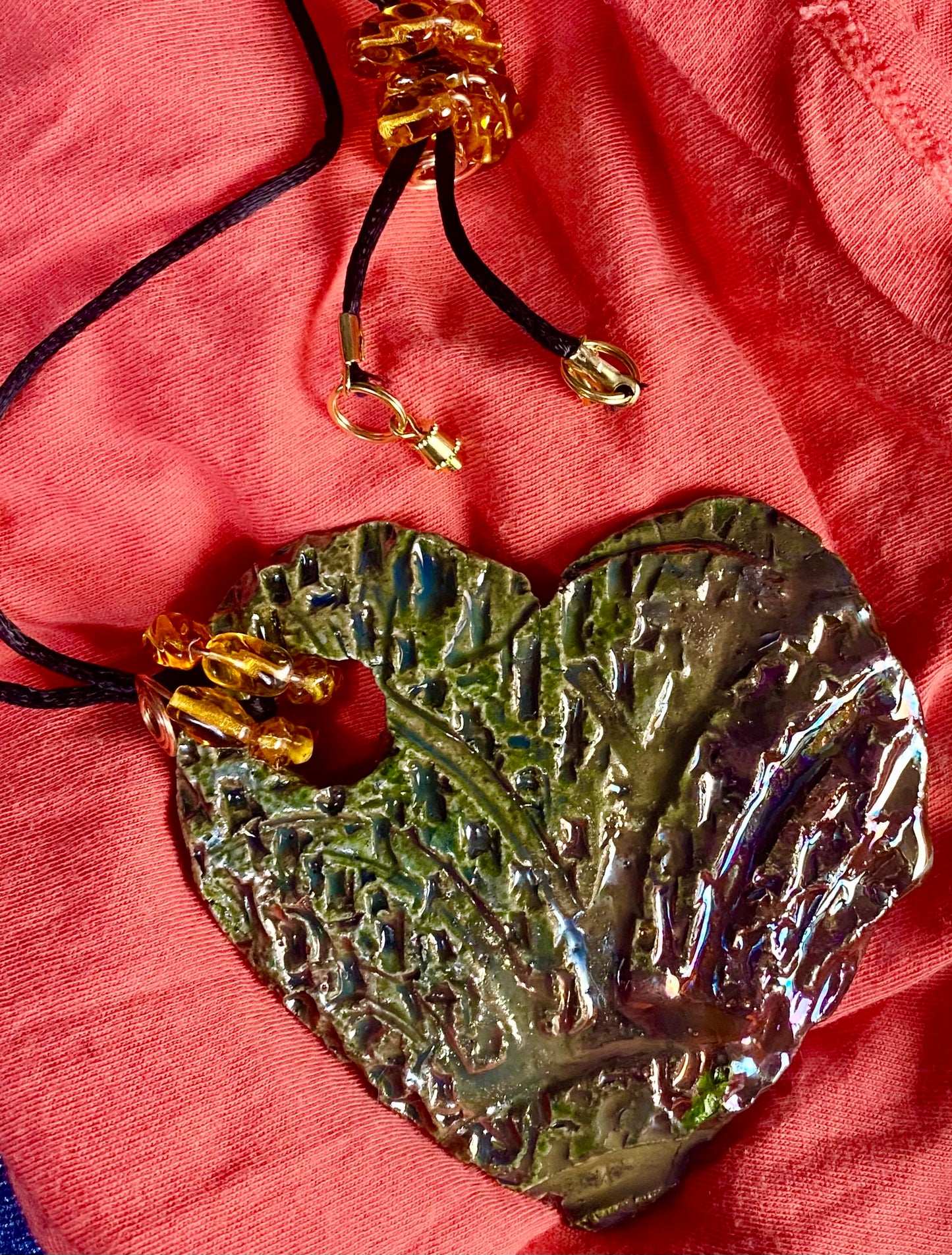 Have A Heart ! Each heart pendant is handmade with love! It is 3"x 3" and weighs approx. 3ozs. This pendant has an alligator green and gold metallic raku glazes that renders a unique translucent patina. The heart has a textured pattern. It holds a spiral of amber mini beads on a spiral copper wire. This pendant has a nice 12" black suede cord!