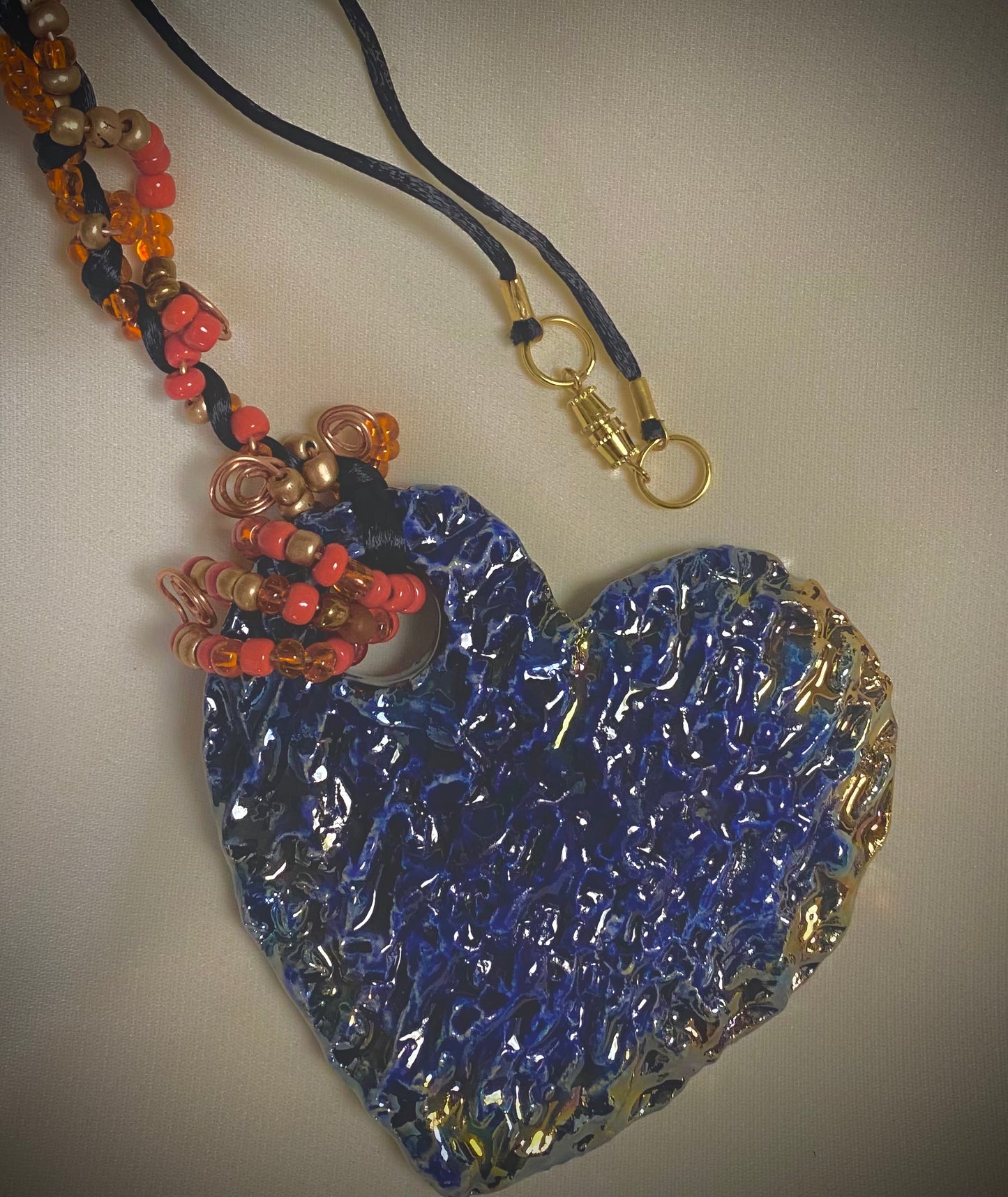 Have A Heart ! Each heart pendant is handmade with love! It is 3"x 3" and weighs approx. 3ozs. This pendant has a blue and gold metallic raku glazes that renders a unique translucent patina. The heart has a textured pattern . It holds a spiral of orange and red mini beads on a spiral copper wire. This pendant has a nice 12" black suede cord!