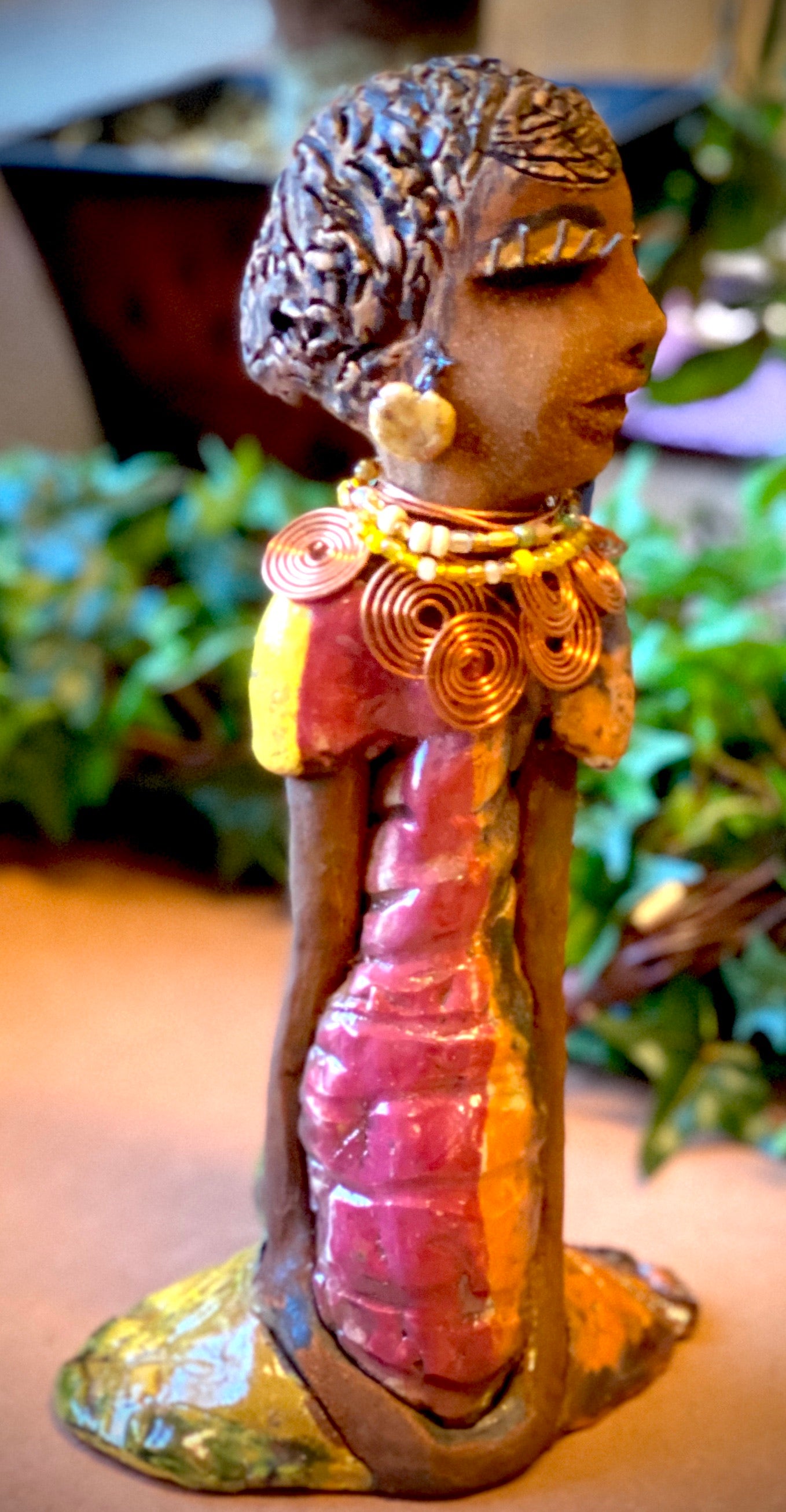 Keeba long loving arms rest beside her multicolored metallic dress. She wears a spiral copper necklace. Keeba is a sophisticated lady that will grace your home.