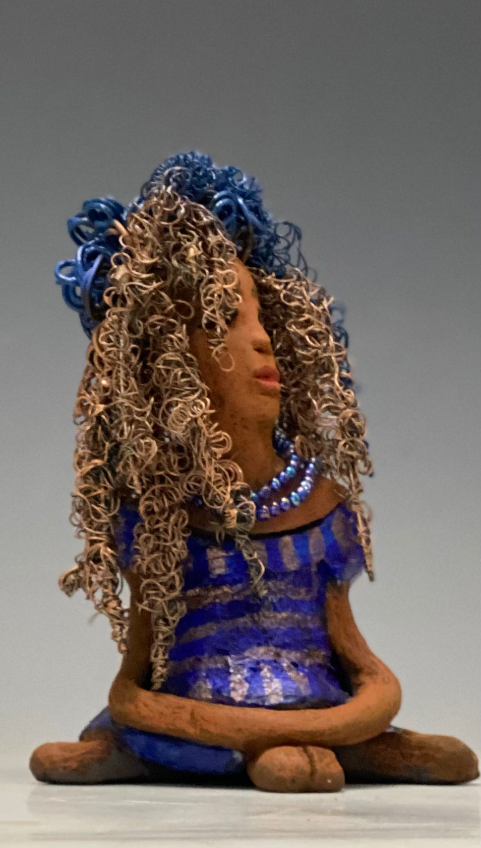 Sherrie stands 6" x 4" x 4.5" and weighs 12.6 ozs. She has a lovely honey brown complexion with reddish brown lips. Sherrie's hairstyle is made up of over 75 feet of twisted 24 gauge wire. Sherrie has a striped metallic copper and blue glazed dress. She wears a aqua blue beaded necklaces. With eyes wide opened, Sherrie has hope of finding a new home. She will make an excellent starter piece from the HerDew collection!