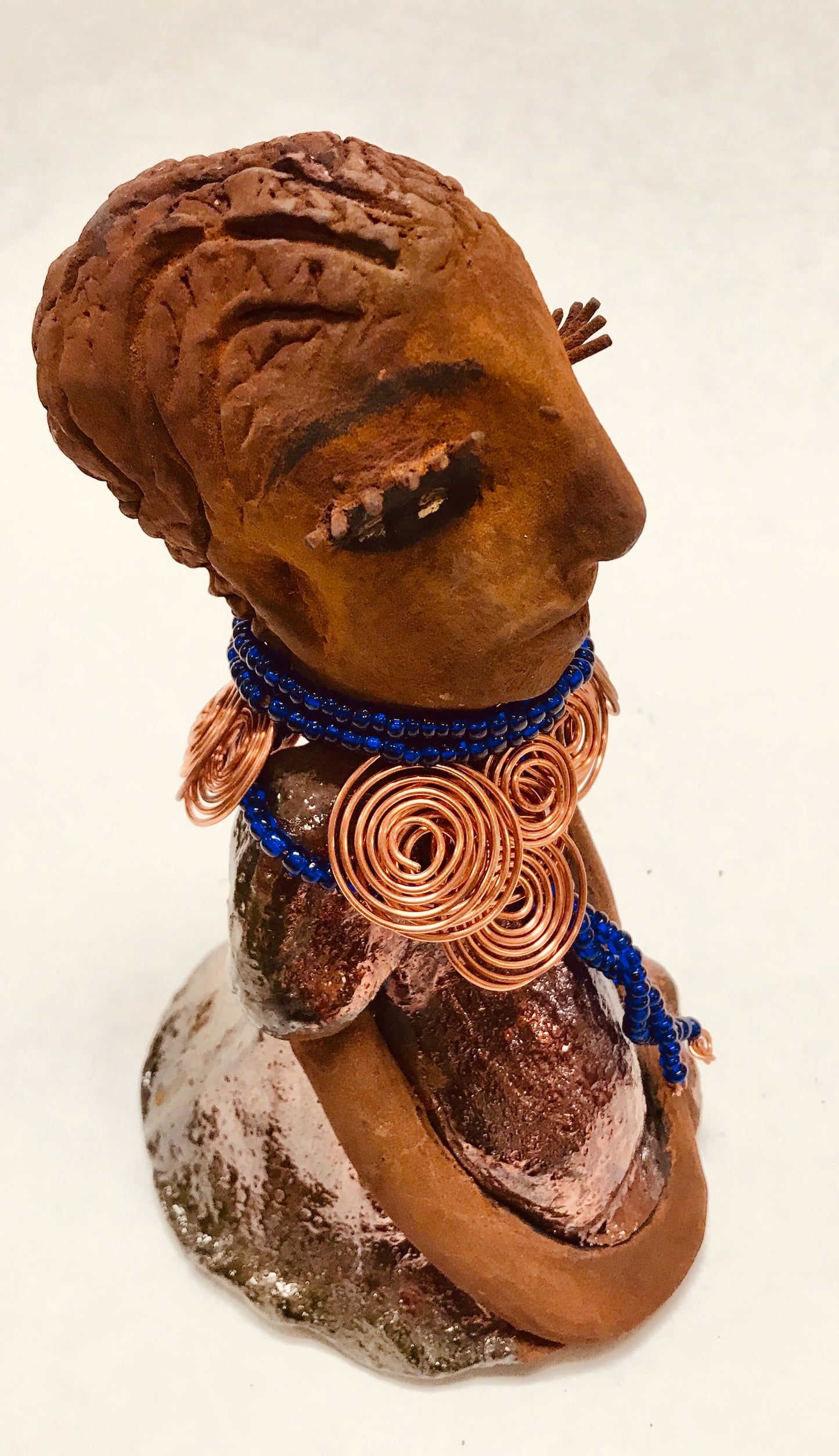 Tattayana stands 8" x 4.5" x 5" and weighs 1.02 lbs. She has a lovely honey brown complexion with reddish brTattayanaown lips. She has a short braided hairstyle. Tattayana has a colorful metallic antique copper glazed dress. She wears spiral copper wire necklaces on top of an aqua blue beaded collar. Tattayana has her long loving arms rest at her side. With eyes wide opened,Tattayana has hopes of finding a new home.