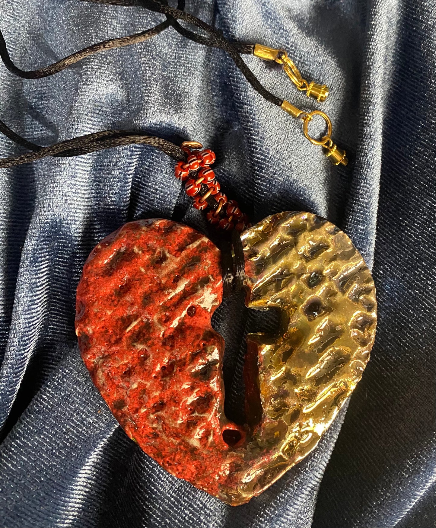 Have A Heart ! Each heart pendant is handmade with love! It is 3"x 3" and weighs approx. 3ozs. This pendant has a ruby red and gold metallic raku glazes that renders a unique translucent patina. The heart has a textured pattern with a cut out cross in the center.. It holds a spiral of ruby red mini beads on a spiral copper wire. This pendant has a nice 12" black suede cord!