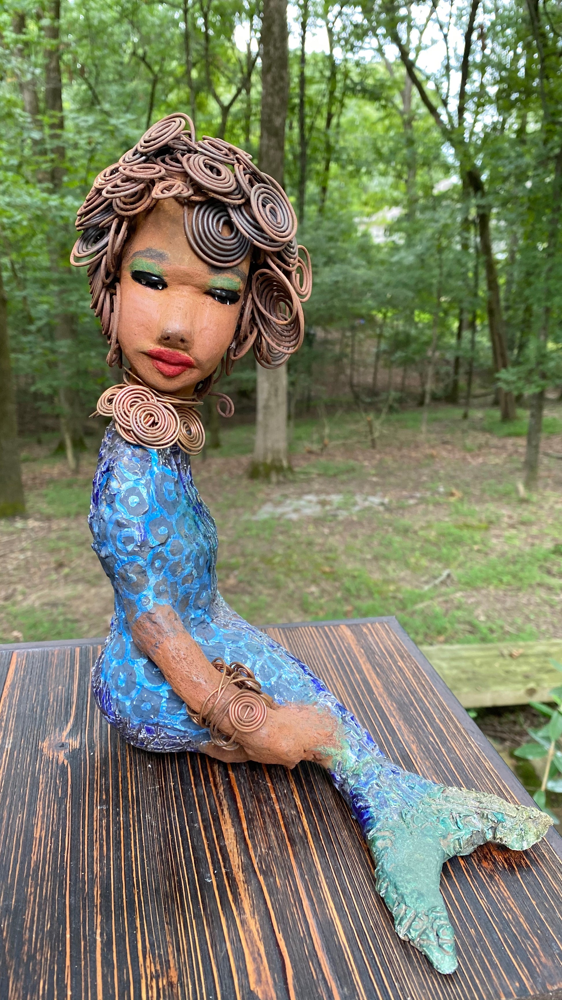 Meet Shelia E.! She is such a Lady I mean Mermaid!    Shelia stands 12" x 10" x 4" and weighs 3.13 lbs. Shelia has a two tone honey brown complexion. She has over 15 feet of spiral wire hair which took over two hours to style. Shelia wears a textured sky blue swimsuit Her layered spiral copper necklace hangs above her long loving arm. Shelia is such a ladylike Mermaid. She sits tall and proud. Compare her to Harmony the mermaid. Give Shelia or Harmony a special place to sit in your home!
