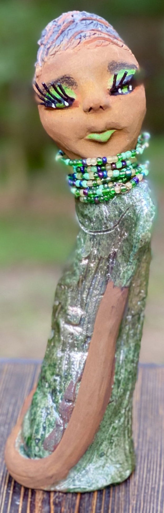 Meet Marissa! Marissa stands 11.5" x 3" x 3.5" and weighs 2.5 lbs. She has a lovely honey brown complexion with reddish brown lips. She has a braided short black clay hairstyle.  Marissa has a colorful metallic copper green antique glazed dress. She wears the world's longest eyelashes. With  her green eyes slightly opened, Marissa has hope of finding her way into your home.