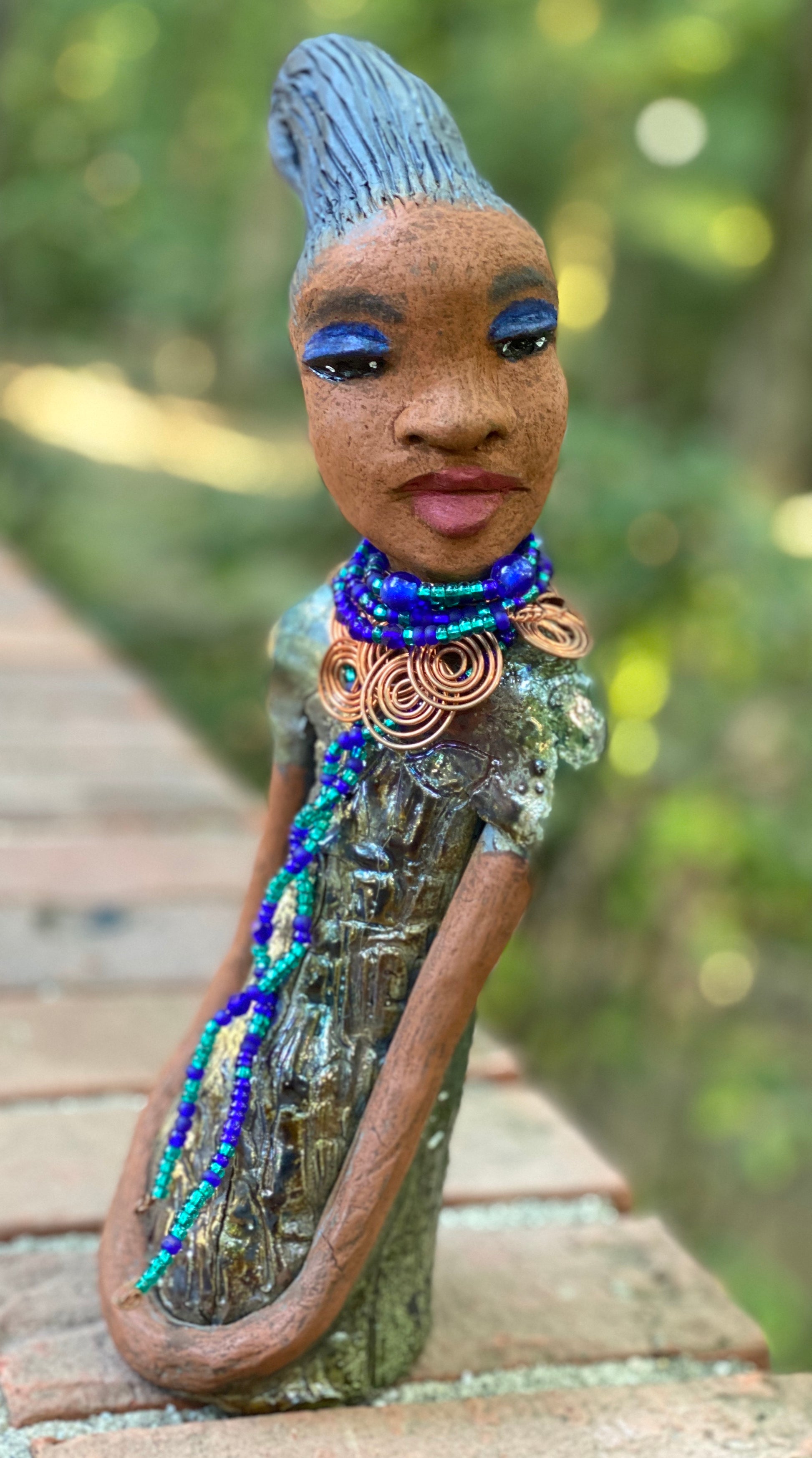 Meet  Emma Again! Emma went and got her a makeover too. She was jealous of Eonna! Emma stands 12.5" x 3. 5" x 4" and weighs 2.04 lbs. She has a lovely honey brown complexion with reddish brown lips. She has a braided clay hairstyle.  Emma has a colorful metallic green antique copper glazed dress. She wears a spiral copper wire necklace on top of a multicolored blue beaded collar. Check out Emma before and after pics. With eyes wide opened,  Emma has hopes of finding  her way into your home!