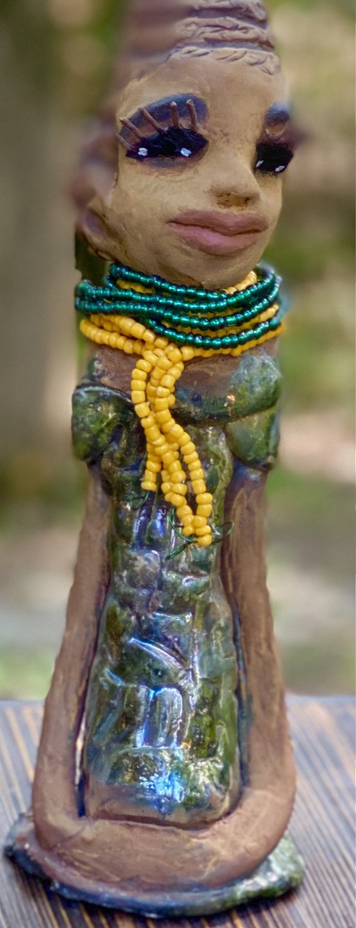 Meet Jazmyne! Jazmyne stands 11" x 4" x 4" and weighs 2.5 lbs. She has a lovely honey brown complexion with  reddish brown lips. She has a braided hairstyle.  Jazmyne has a colorful metallic green antique copper glazed dress. She wears a bright yellow beaded necklace. With long lashes and eyes wide opened, Jazmyne has hopes of finding a new home.    Jazmyne  will attract and spark conversation with guest in your home!