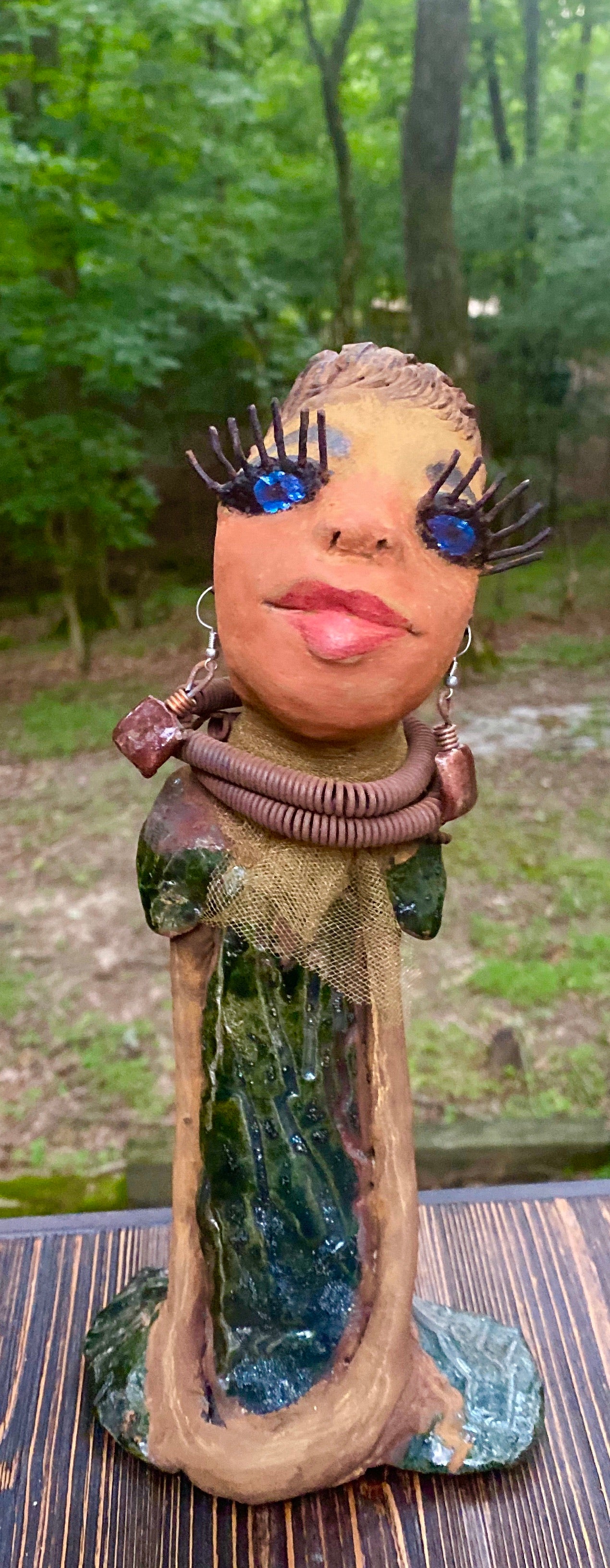 Meet Catera! Catera stands 10" x 4" x 4" and weighs 2.7 lbs. She has a lovely honey brown complexion with  reddish brown lips. She has a braided hairstyle.  Catera has a colorful metallic green antique copper glazed dress. She wears a yellow bead necklace with raku beads. Her long loving arms are resting at her side. With long lashes and eyes wide opened, Catera has hopes of finding a new home.