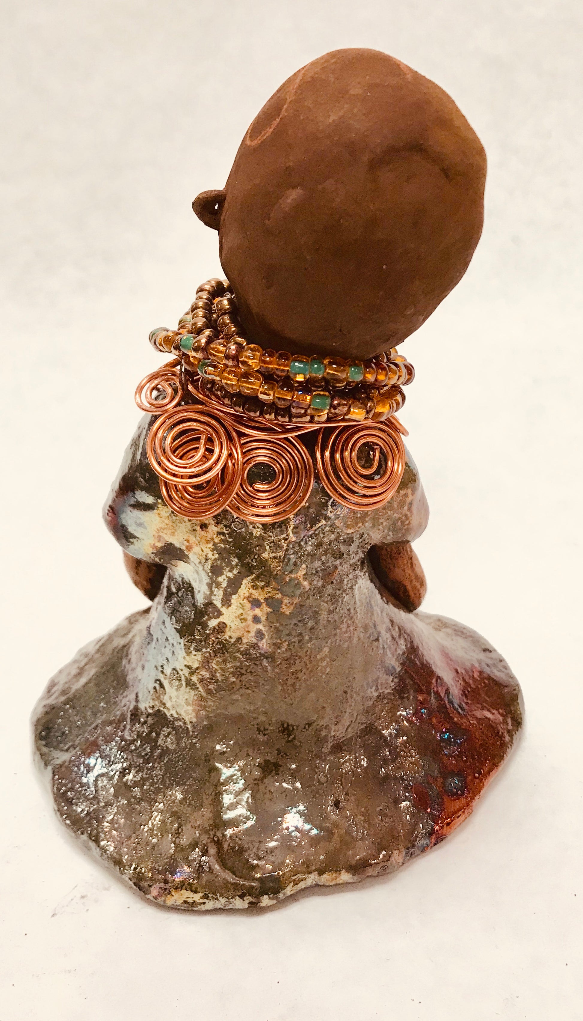 Meet Faye! Faye stands 7" x 5" x 4" and weighs 2.3 lbs. She has a lovely two tone honey brown complexion with  chocolate brown lips. She has a braided hairstyle.  Faye has a colorful metallic green antique glazed dress. She wears an awesome beaded collar with a copper spiral necklace. Her long loving arms rest at her side. With eyes wide opened, Faye has hopes of finding a new home.