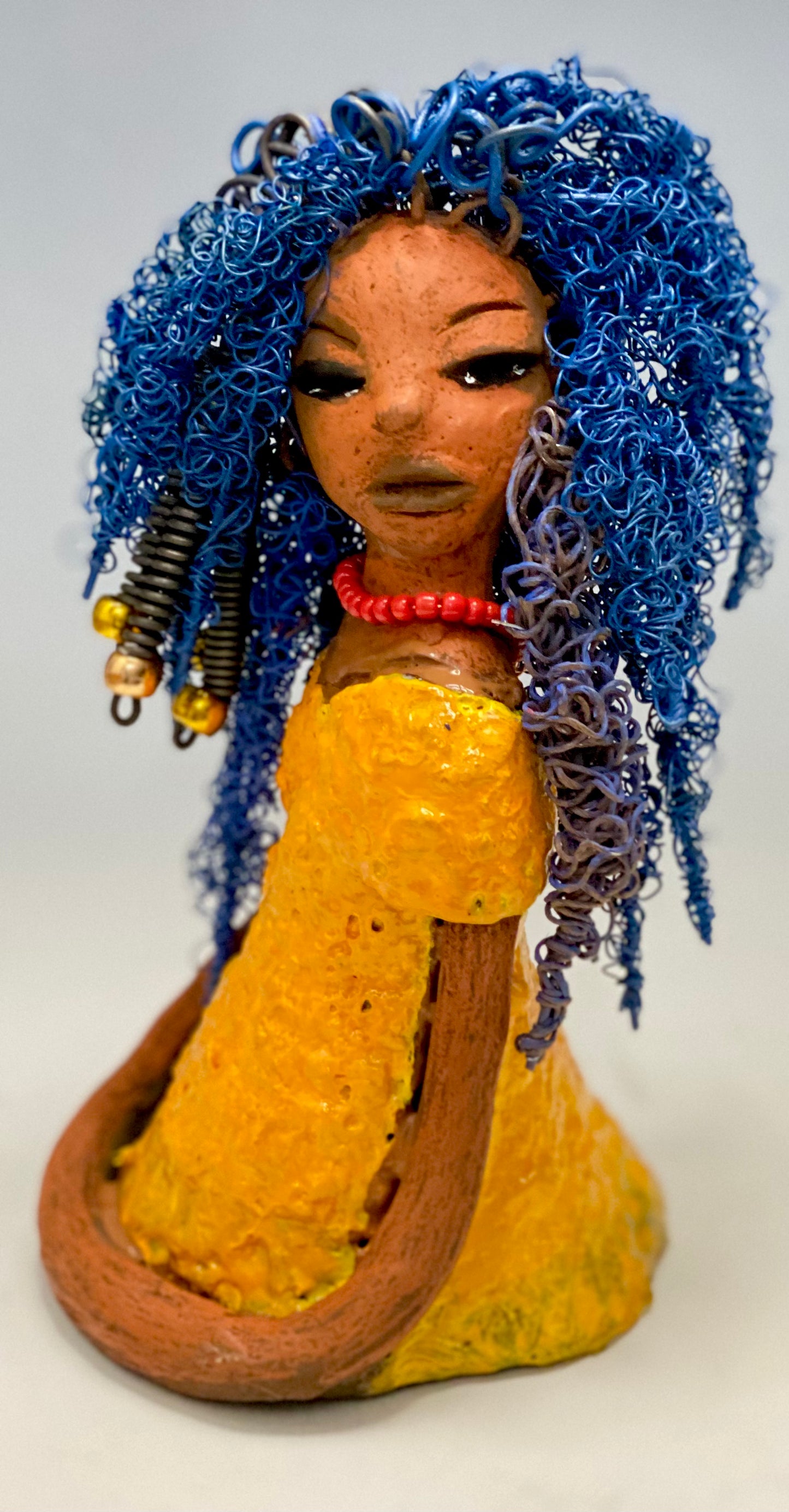 Makeba stands 8" x 5" x 5" and weighs 1.4 lbs. She has a lovely honey brown complexion with cocoa red lips. She has long twisted blue wire locs hairstyle waist down! Makeba has a sunset yellow red glazed dress. She has over 75 feet of 16 and 24 gauge blue wire for hair. It took over 5 hours just to do her hair! With eyes wide opened and a subdue look, Makeba has hope of finding a new home.