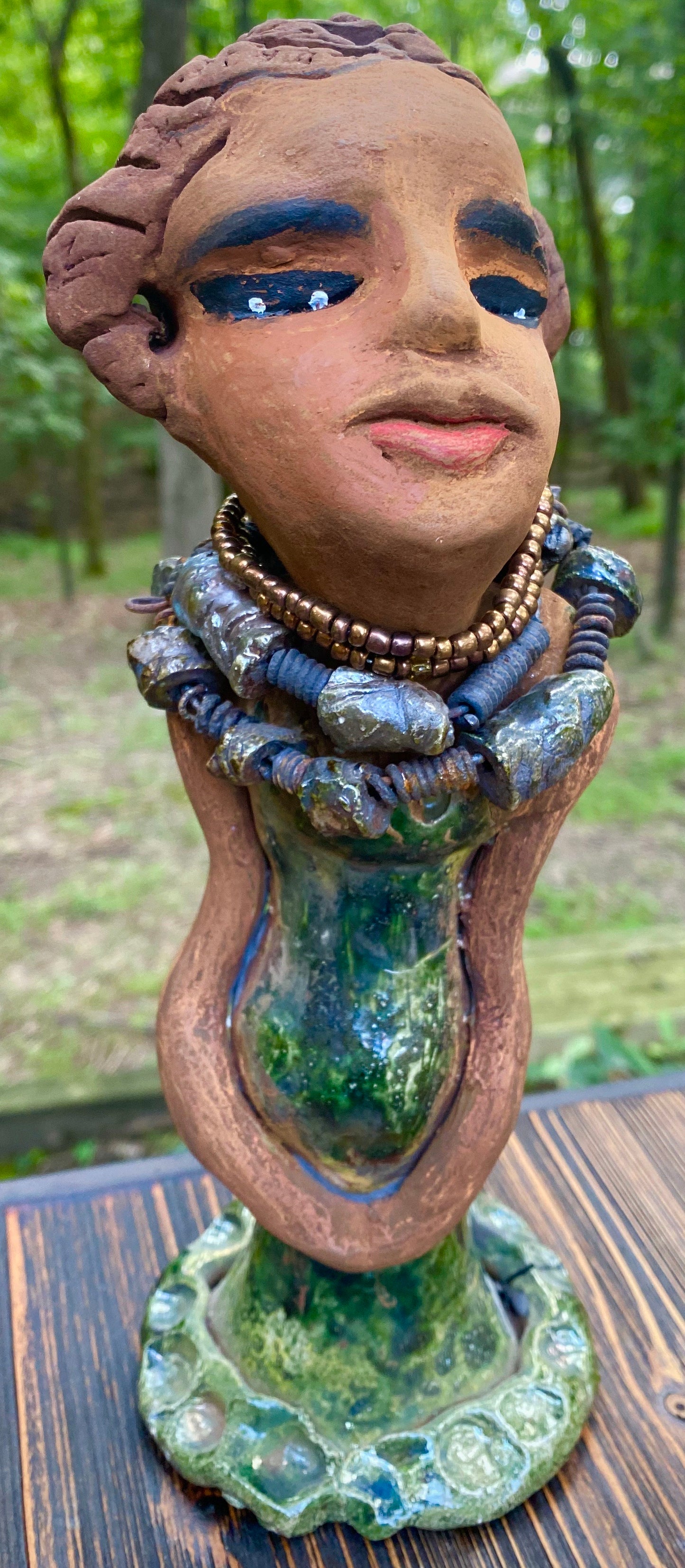 Greta! Greta stands 11" x 4" x 4" and weighs 2.5 lbs. She has a lovely honey brown complexion with reddish brown lips. She has a braided hairstyle. Gretaya has a colorful metallic green antique copper glazed dress. She wears two raku beaded necklaces. With long eyes slightly opened, Greta has hopes of finding a new home.