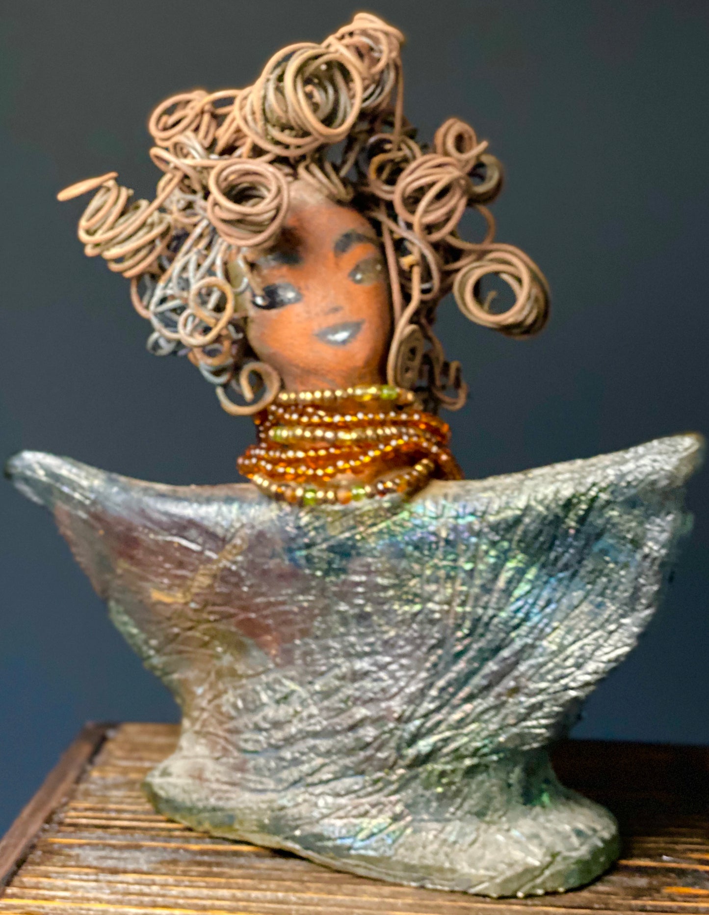 Lizzie Got Big Hair! Lizzie stands 8" x 7" x 2.5" and weighs 1 lb. Her robe is textured with a multicolored metallic copper glaze. Lizzie has really Big Hair. The hair is over 25 feet of curly 16 gauge wire. Her complexion is a lovely cocoa brown. Lizzie has an angelic pose with her arms up in adoration. Give Lizzie a specail place in your home!