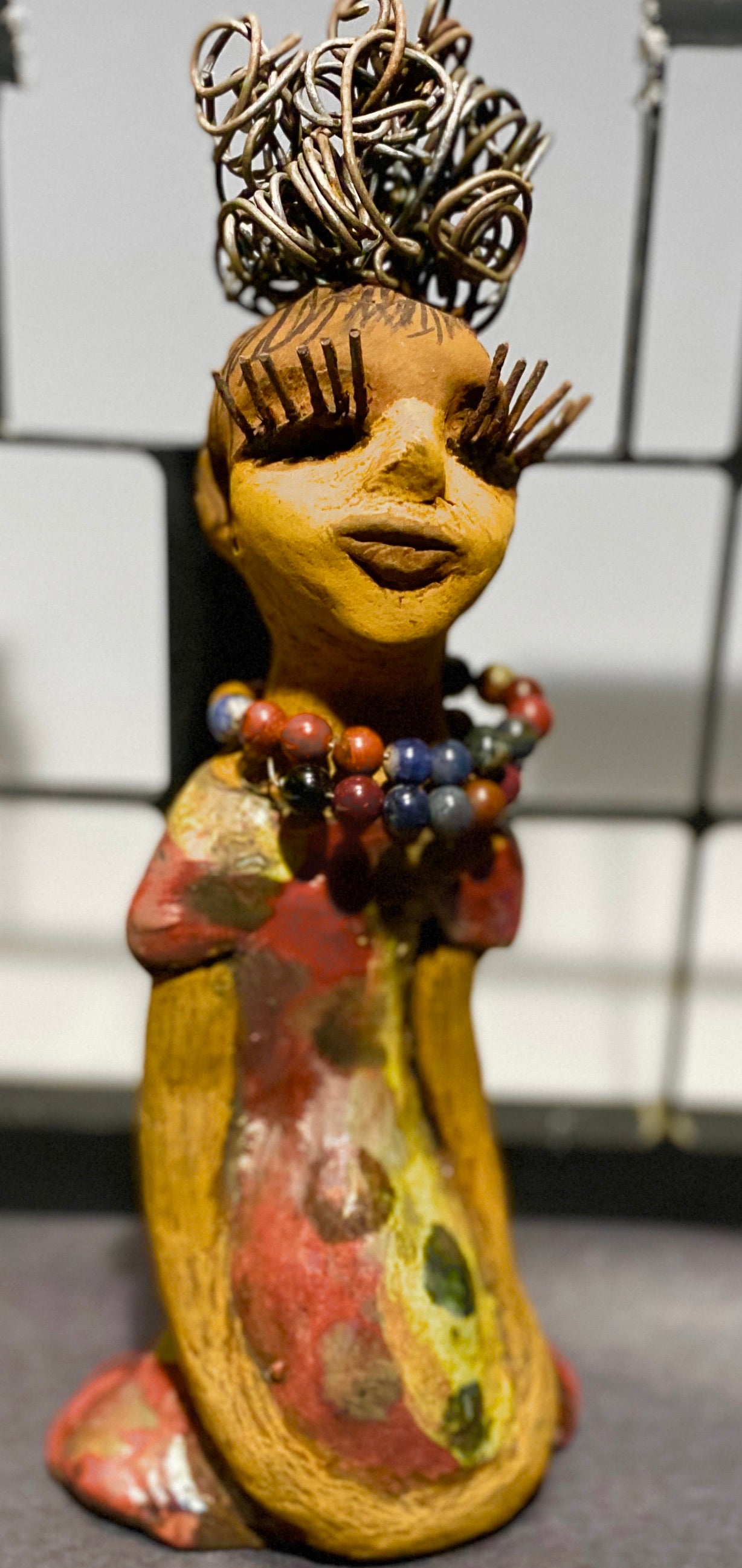 You know someone like Tiffanie. One who reaps elegance and sophistication! Tiffanie stands 9”x 4" x 4" and weighs 1.03 lbs. She has a two tone light beige complexion with 2 feet of 16 gauge spiral coiled wire hair. Tiffanie metallic copper red and yellow dress is accented by a multicolored beaded necklace. Tiffanie’s long lashes and black eye shadow gives her a distinguished mystical look.