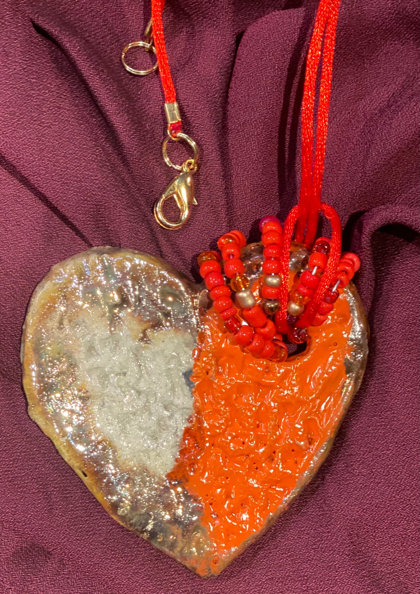 Have A Heart ! Each heart pendant is handmade with love! It is 3"x 3"and weighs approx. 3ozs. This pendant has a red violet and gold metallic raku glazes that renders a unique translucent patina. The heart has a textured pattern . Both sides are are different and equally beautiful! It holds a spiral of red and gold mini beads on a spiral copper wire. This pendant has a nice 12" red rattail cord!