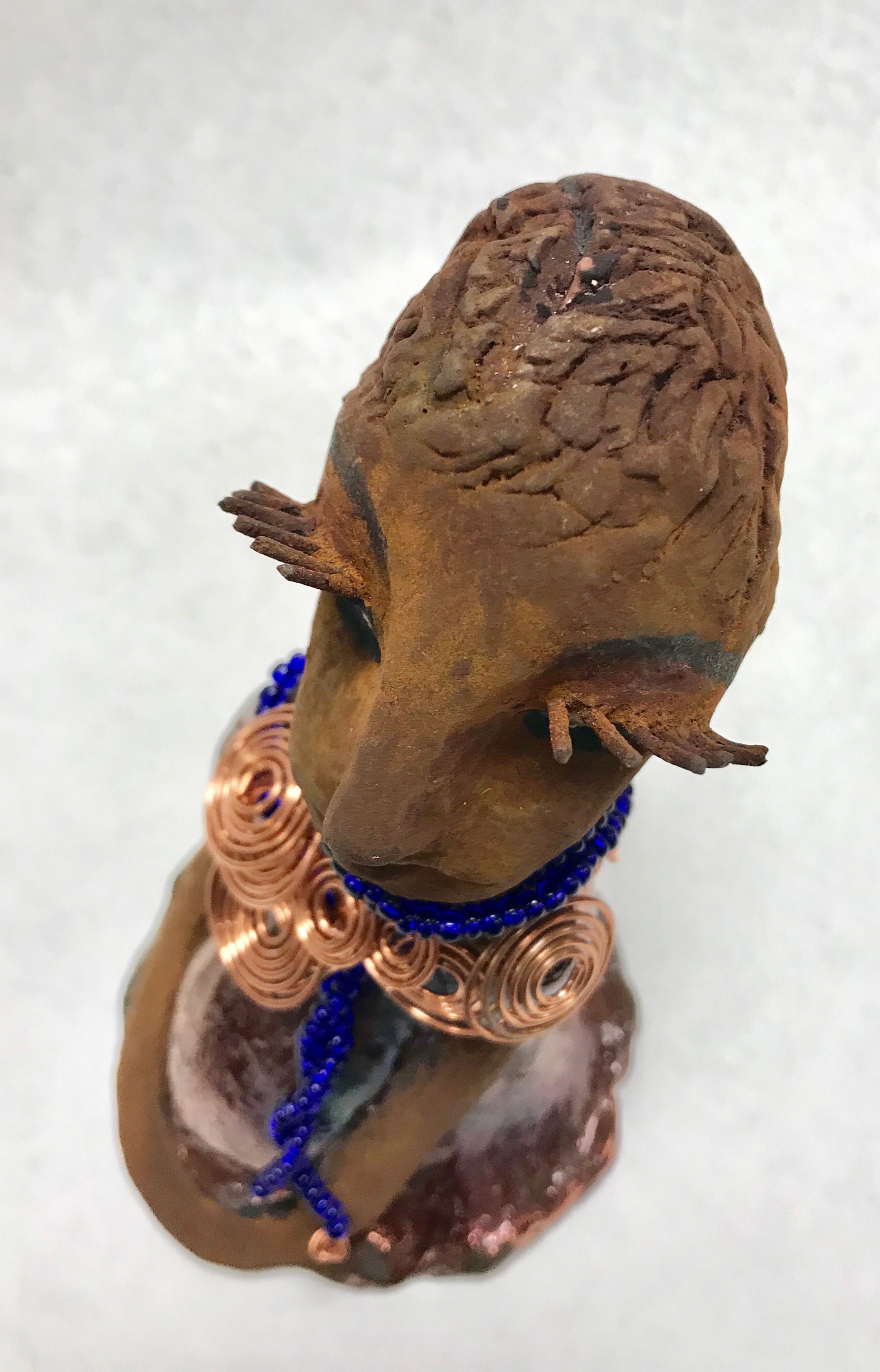 Tattayana stands 8" x 4.5" x 5" and weighs 1.02  lbs. She has a lovely honey brown complexion with reddish brTattayanaown lips. She has a short braided hairstyle.  Tattayana has a colorful metallic antique copper glazed dress. She wears spiral copper wire necklaces on top of an aqua blue beaded collar.  Tattayana has her long loving arms rest at her side. With eyes wide opened,Tattayana  has hopes of finding a new home.