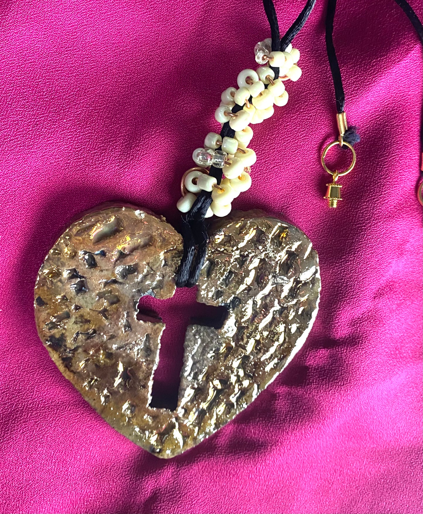 Have A Heart ! Each heart pendant is handmade with love! It is 3"x 3" and weighs approx. 3ozs. This pendant has an off white and gold metallic raku glazes that renders a unique translucent patina. The heart has a textured pattern with a cut out cross in the center.. It holds a spiral of off white mini beads on a spiral copper wire. This pendant has a nice 12" black suede cord!