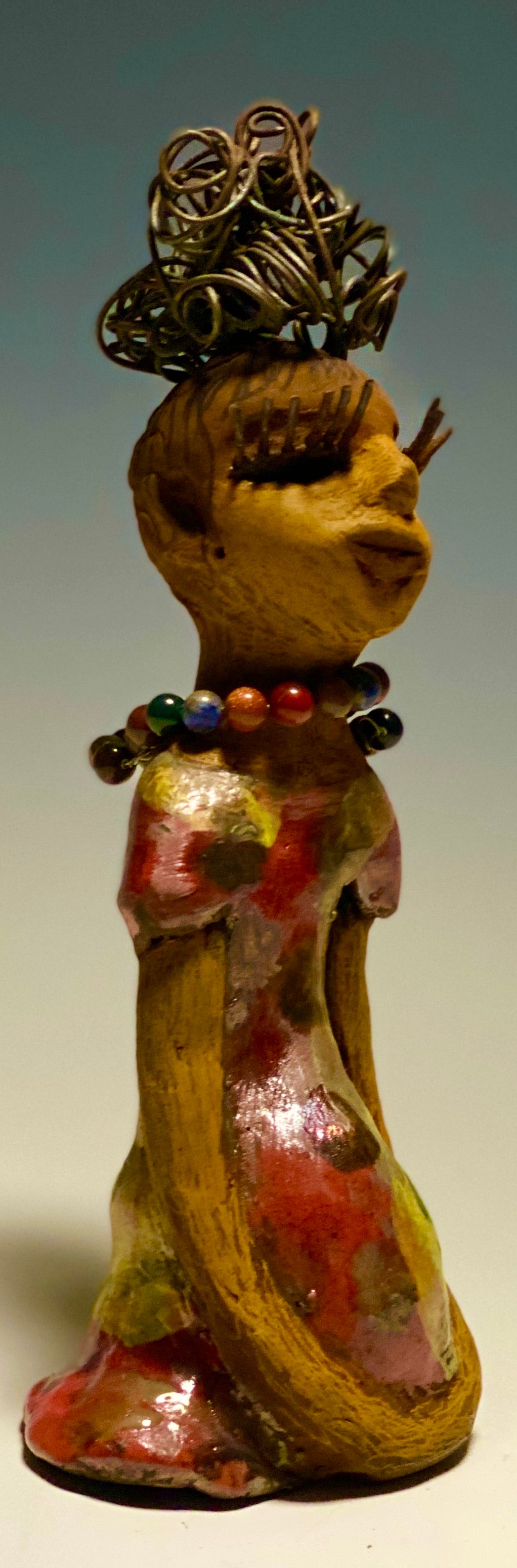 You know someone like Tiffanie. One who reaps elegance and sophistication!  Tiffanie stands 9”x 4" x 4" and weighs 1.03 lbs.  She has a two tone light beige complexion with 2 feet of 16 gauge spiral coiled wire hair.  Tiffanie metallic copper red and yellow  dress is accented by a multicolored beaded necklace. Tiffanie’s long lashes and  black eye shadow gives her a distinguished mystical look.