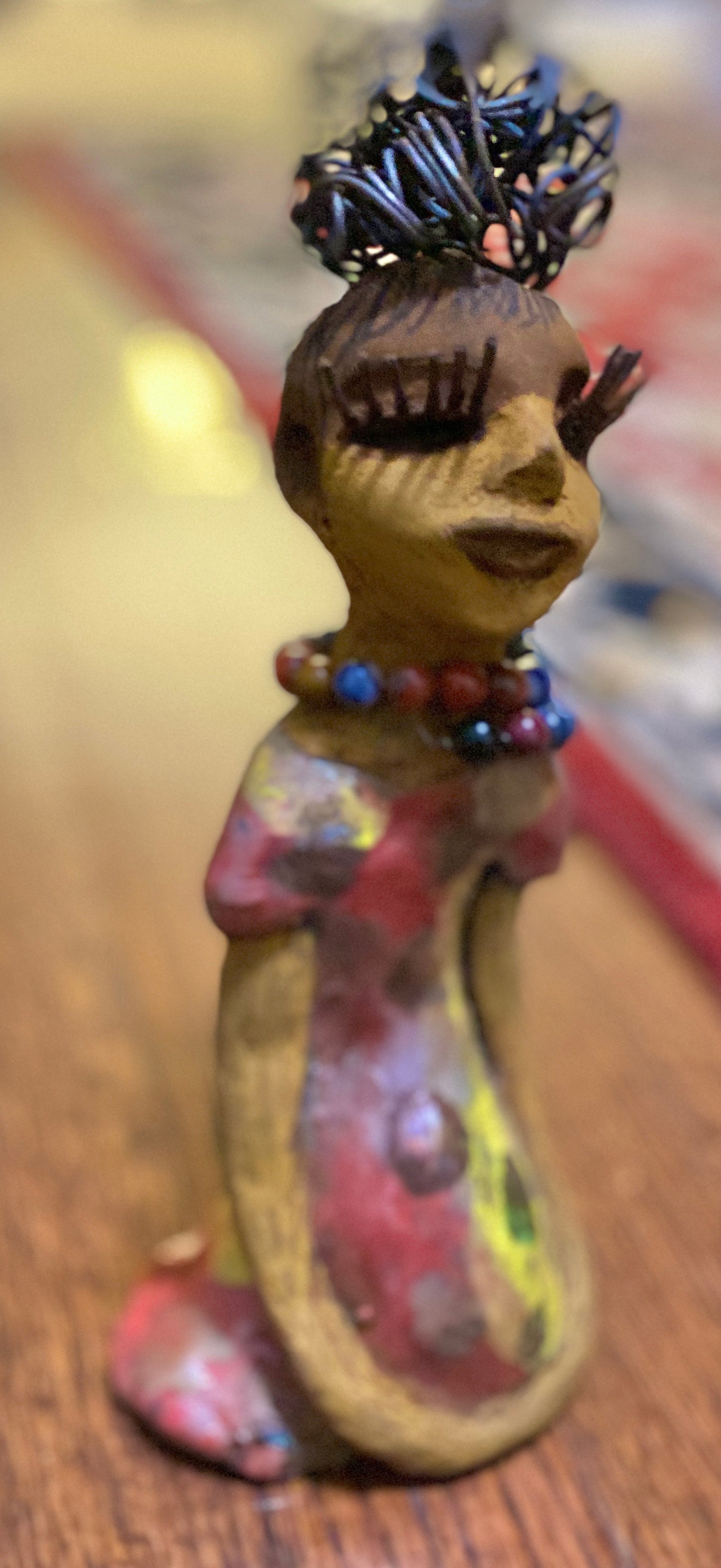 You know someone like Tiffanie. One who reaps elegance and sophistication! Tiffanie stands 9”x 4" x 4" and weighs 1.03 lbs. She has a two tone light beige complexion with 2 feet of 16 gauge spiral coiled wire hair. Tiffanie metallic copper red and yellow dress is accented by a multicolored beaded necklace. Tiffanie’s long lashes and black eye shadow gives her a distinguished mystical look.