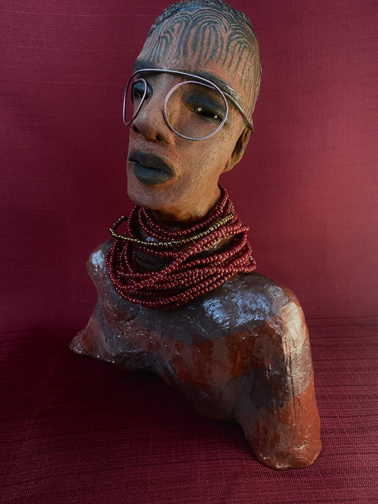 Meet Harriet! Harriet stands 13" x 11" x 5" and weighs 5 lbs. She wears a coral striped dress with a string of ruby red and gold beads. Harriet has a honey brown rust complexion  and distinct eyes. Her eyes  are slightly opened underneath her glasses... She has mixed black and copper streaks of straight corn rolls of clay hair. She has a straight look of concern as to what is about to take place.