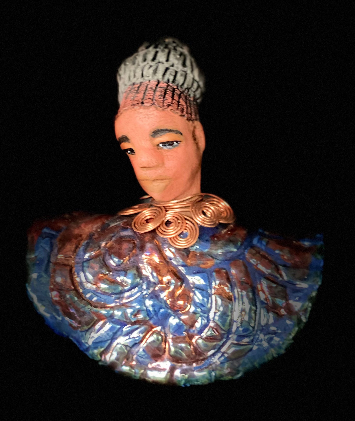 Meet Tia! Tia looks up with joy and anticipation! Tia stands 7" x 6" x 4" and weighs 1.90 lbs. She has a beautiful textured copper and blue robe. Tia has braided clay hair up in a bun. She has a honey brown complexion and soft light brown lips. Tia will make for great conversation in your home. Free Shipping! Check out our Shipping and Return policy