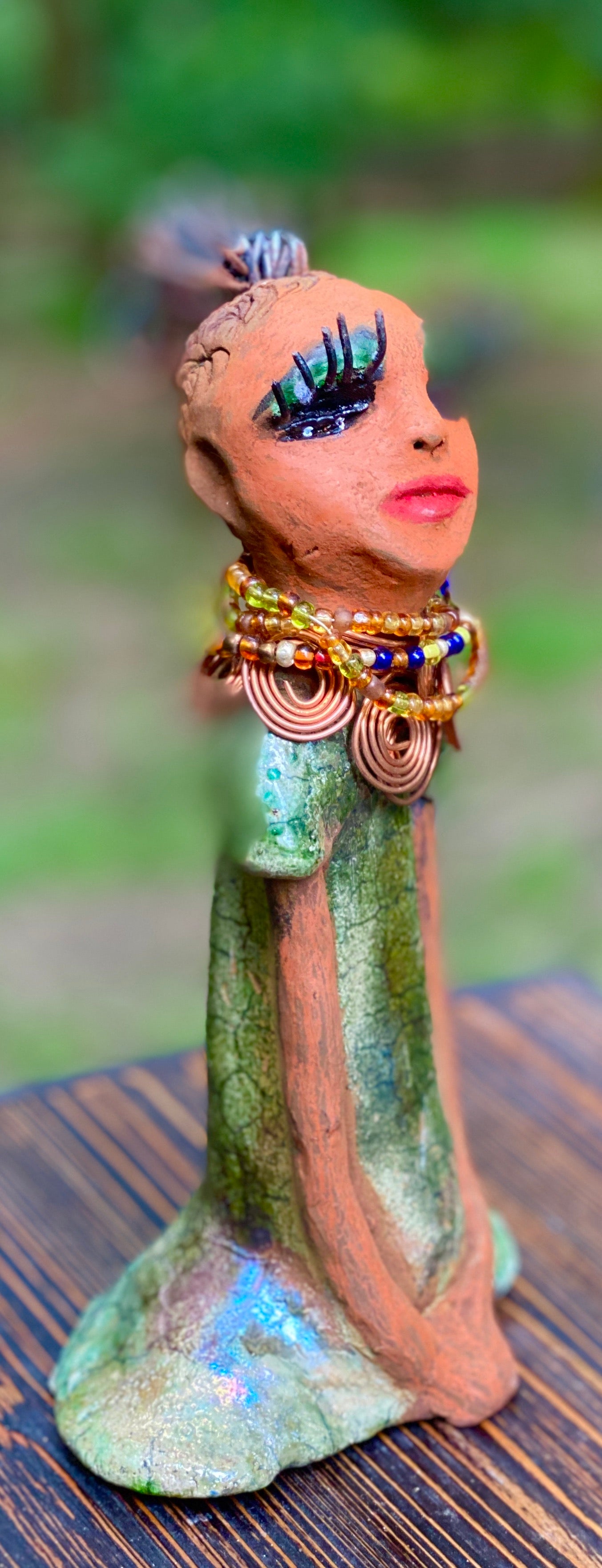 Kaleesia says yes to wire hair and yes to the Herdew tribe. Kaleesia stands 9” x 5" x 2.5" and weighs 1.05 lbs. She has a lovely beige brown complexion with short etched braided clay hair. Kaleesia long loving arms rest beside her multicolored copper green dress. Kaleesia is a sophisticated lady that will grace your home.