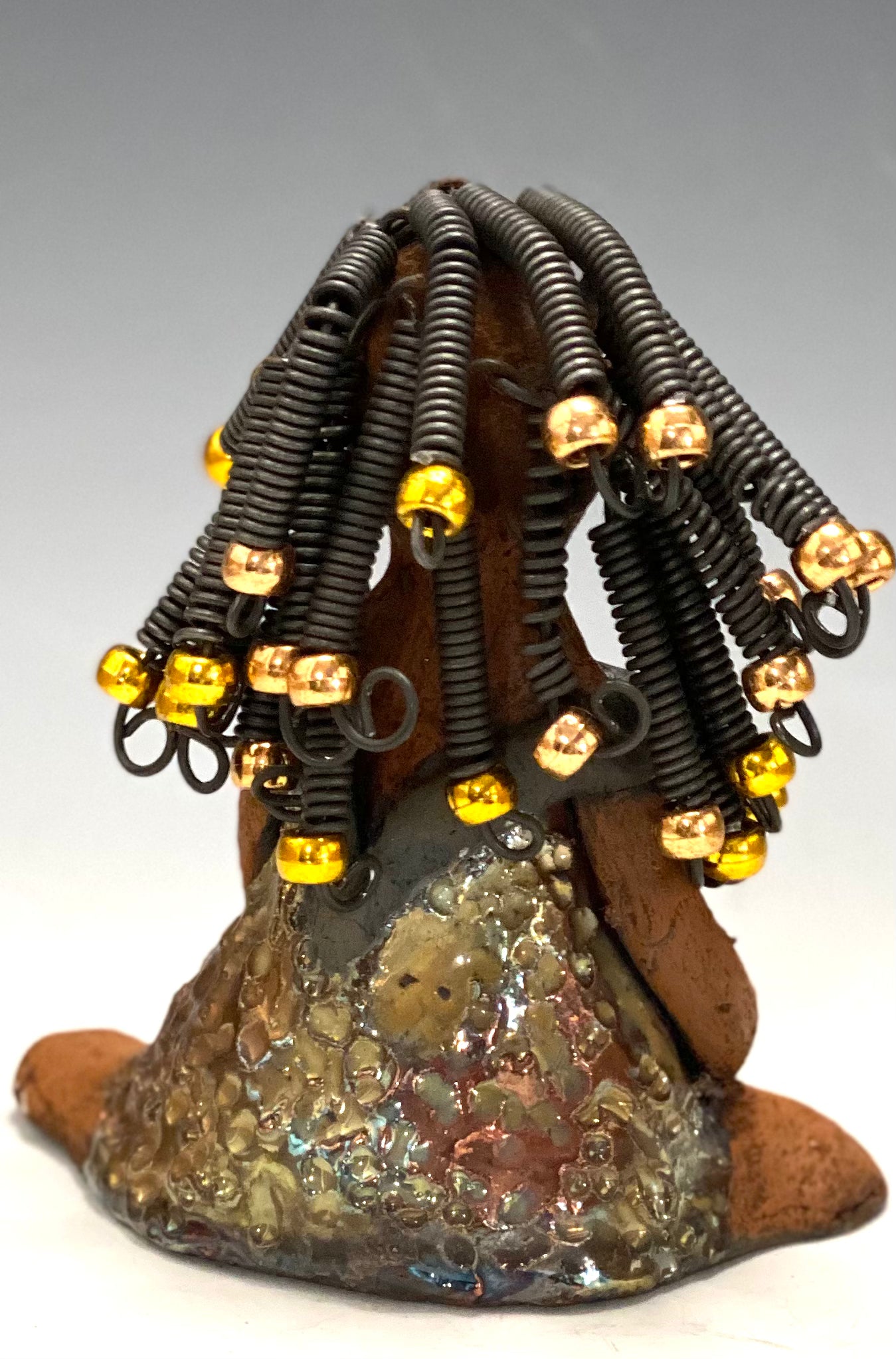 Meet Sadie Sadie stands 5.5" x 4" x 3" and weighs 8.7 ozs. She wears a lovely glossy metallic gold dress.. Sadie has over15 feet of coiled wire hair. Sadie appears to sit in a yoga pose. Her long arms rest at her side. Sadie is a great starter piece from the Herdew Collection!