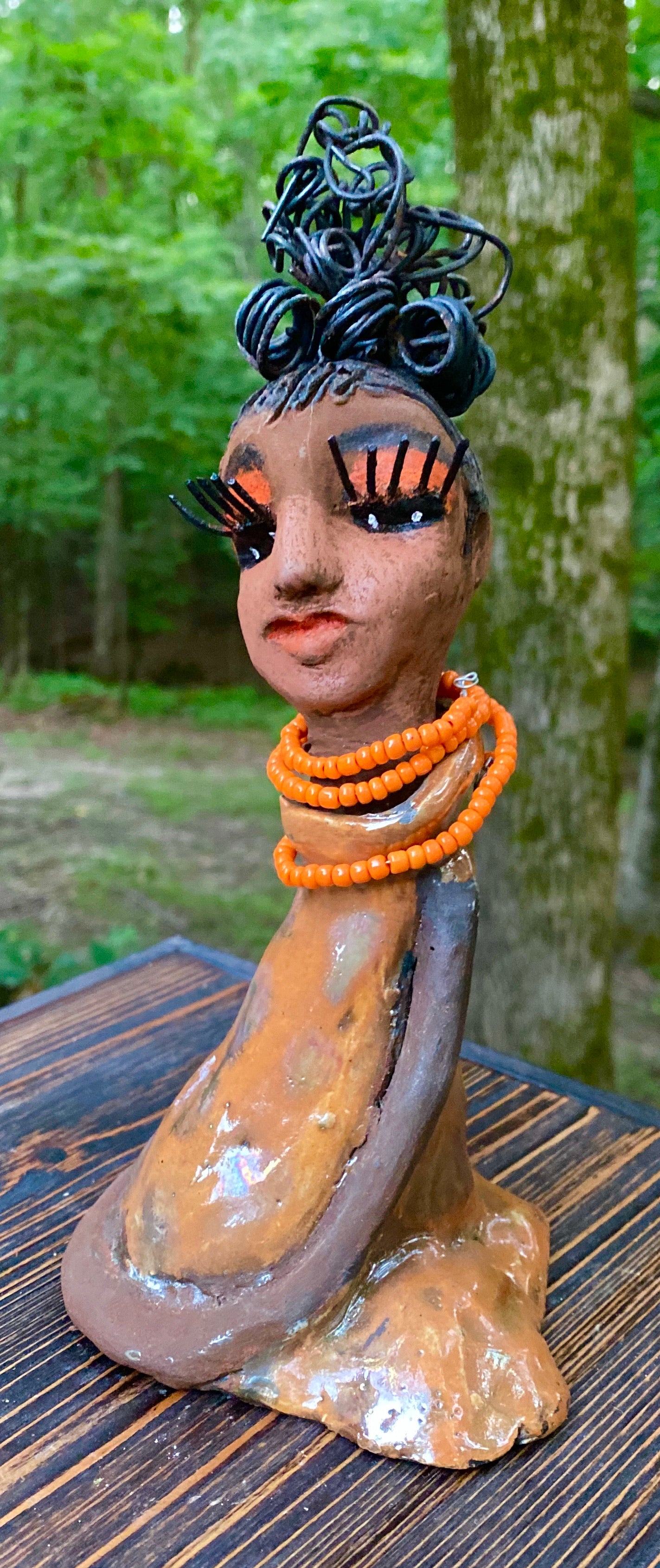 Meet Abimbola ! Abimbola stands 7' x 4"x 2" and weighs 1.3 lb. She has bright eyes and a nice honey brown complexion Abimbola  has over 5 feet of 16 gauge wire hair wrapped in a bun. Her long trademark arms rest at her side. Abimbola dress is a loving glossy orange mix with copper flashes. Abimbola is waiting for you to invite her into your home!