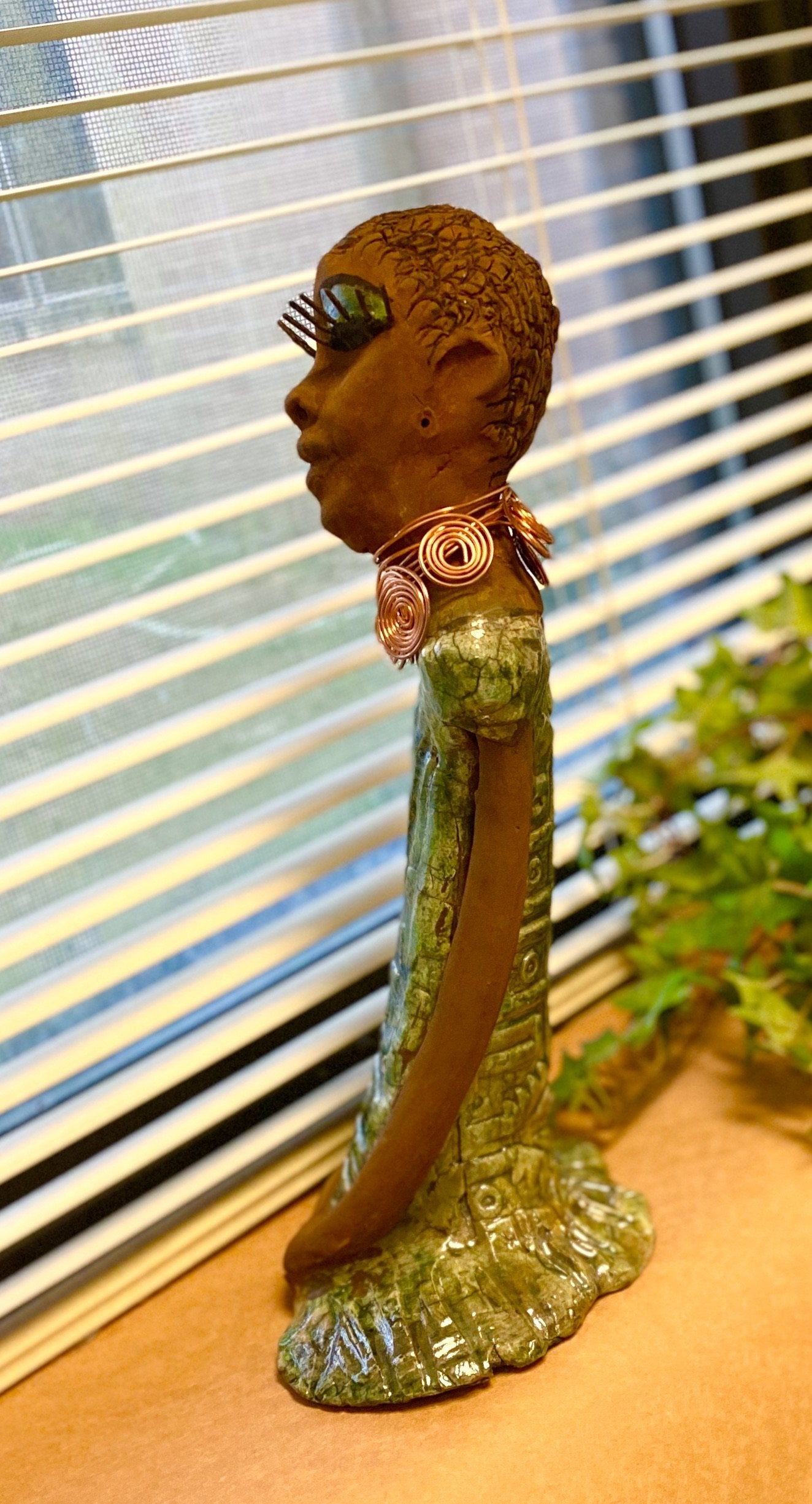 Gabrielle stands 14" x 6" x 5.5" and weighs 2.15 lbs. She has a lovely honey brown complexion with green eye shadow. Her hairstyle is etched in clay with tribal markings. Gabrielle long loving arms rest beside her alligator green dress. She wears a spiral copper necklace. Gabrielle is a sophisticated lady that will grace your home.