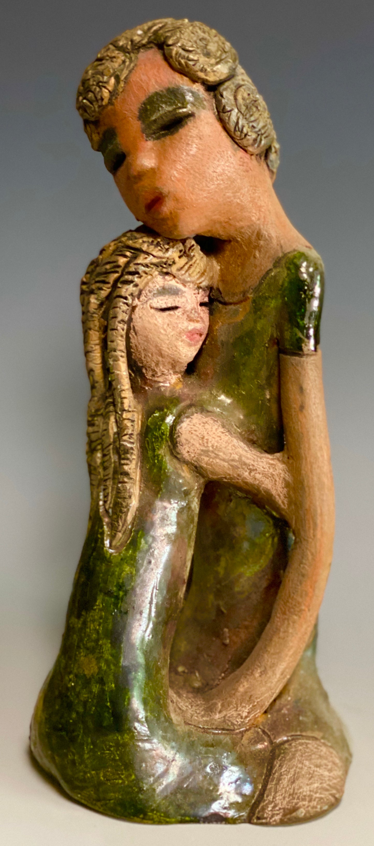 "Hold Me Mama has a very similar look and feel as Girl Talk with my Mom". Hold Me Mama depicts the bond between a mother and child". They stand 10" x 5" x 5" and weighs 2.8 lbs. Mother and Child has honey brown complexions with etched copper colored clay hair. They wear green/ copper raku fired glossy dresses. Mother assures her daughter that everything will be alright!