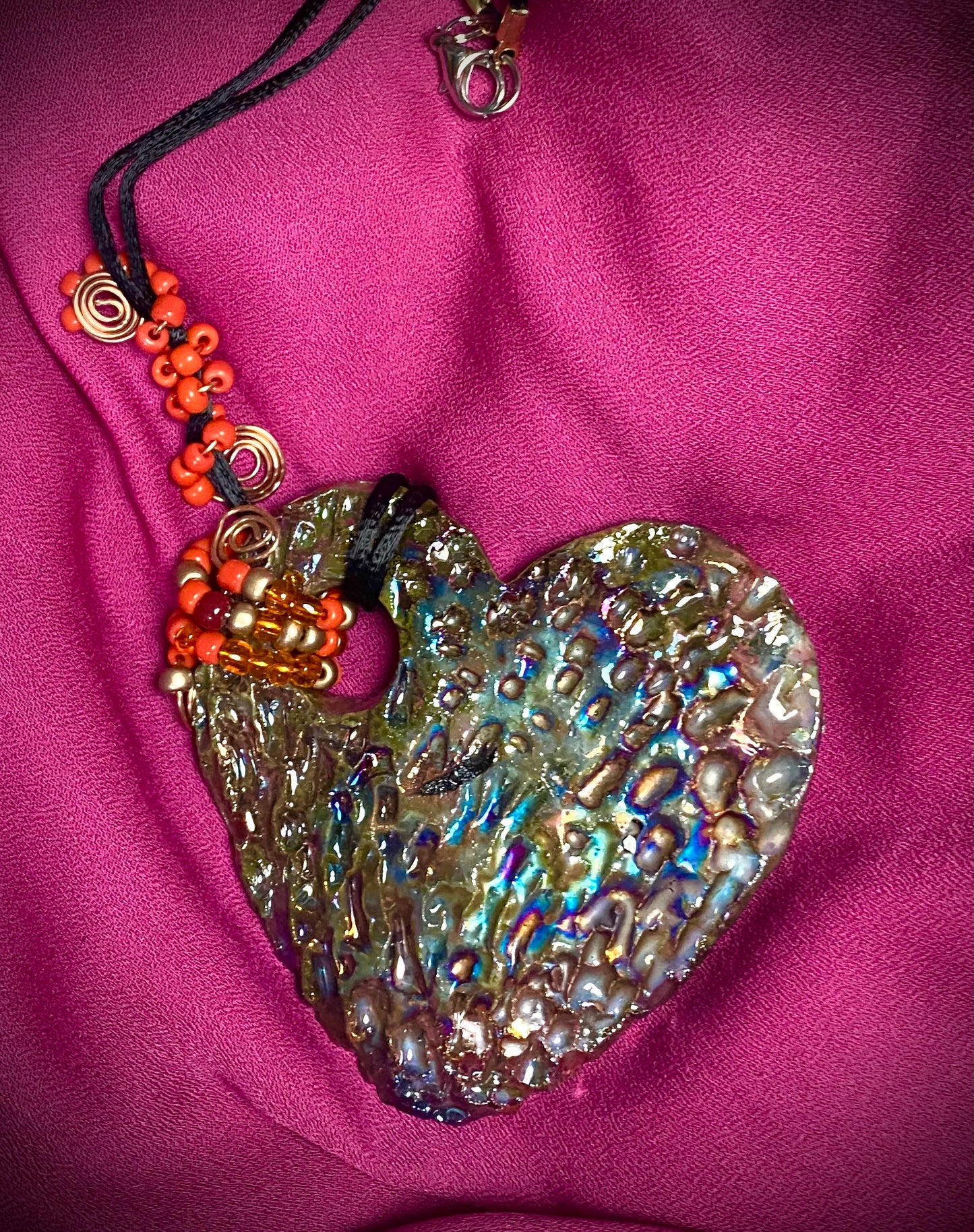 Have A Heart ! Each heart pendant is handmade with love! It is 3"x 3" and weighs approx. 3ozs. This pendant has a copper gold metallic raku glazes that renders a unique translucent patina. The heart has a textured pattern . It holds a spiral of amber and red mini beads on a spiral copper wire. This pendant has a nice 12" black suede cord!