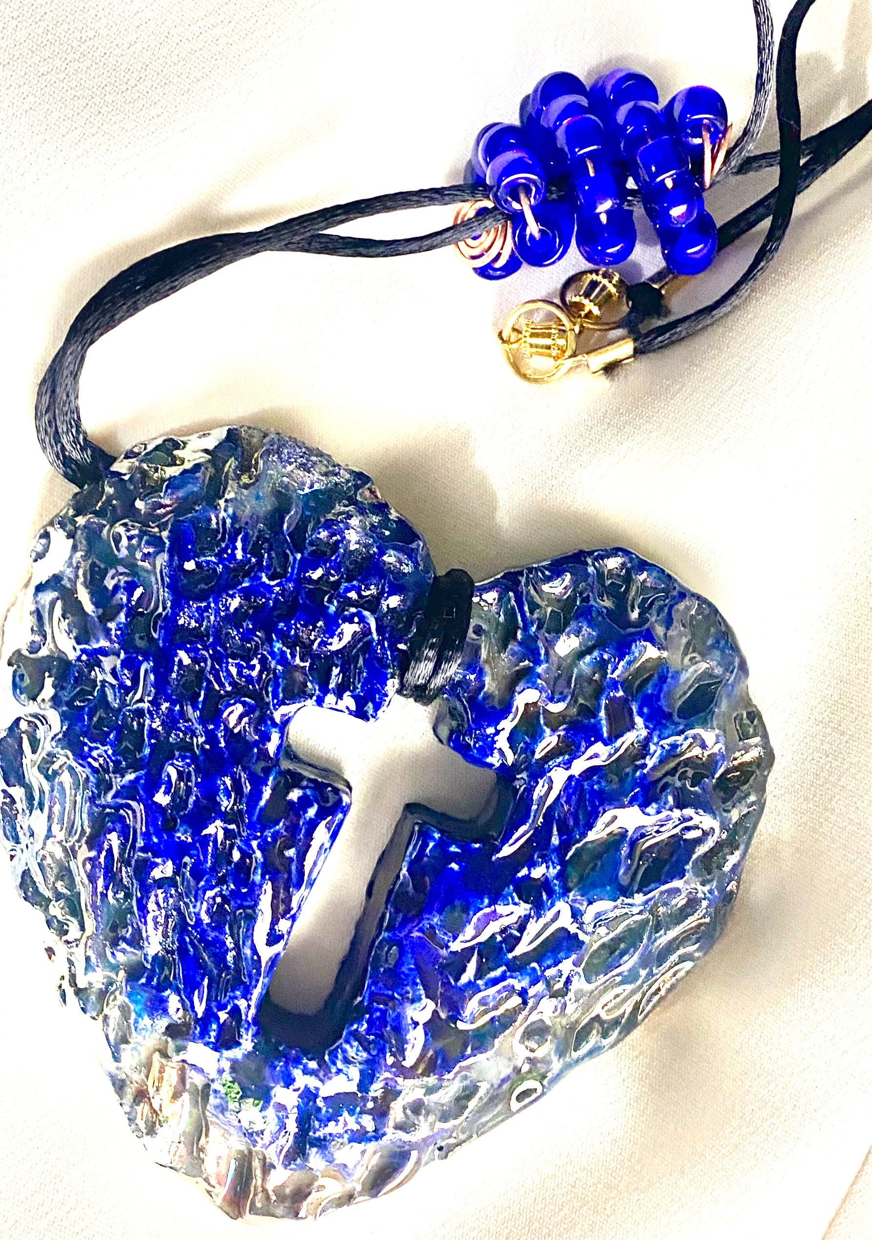 Have A Heart ! Each heart pendant is handmade with love! It is 3"x 3" and weighs approx. 3ozs. This pendant has a royal blue and gold metallic raku glazes that renders a unique translucent  patina. The heart has a cut out cross in the center with a textured  pattern. It holds a spiral of royal blue mini beads on a spiral copper wire. This pendant has a nice 12" black suede cord!