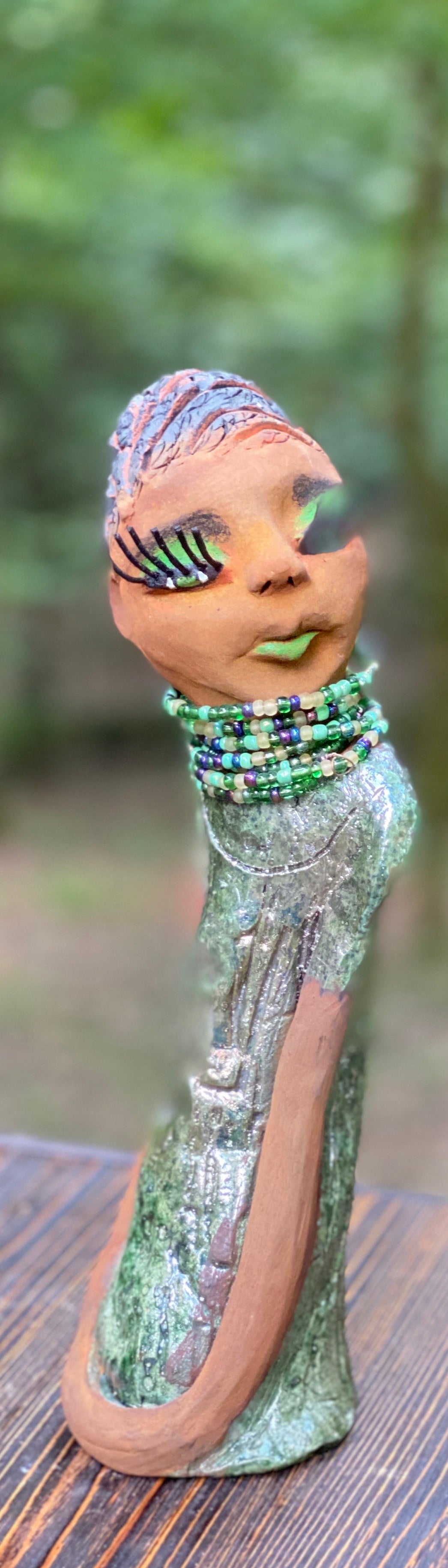 Meet Marissa! Marissa stands 11.5" x 3" x 3.5" and weighs 2.5 lbs. She has a lovely honey brown complexion with reddish brown lips. She has a braided short black clay hairstyle. Marissa has a colorful metallic copper green antique glazed dress. She wears the world's longest eyelashes. With her green eyes slightly opened, Marissa has hope of finding her way into your home.