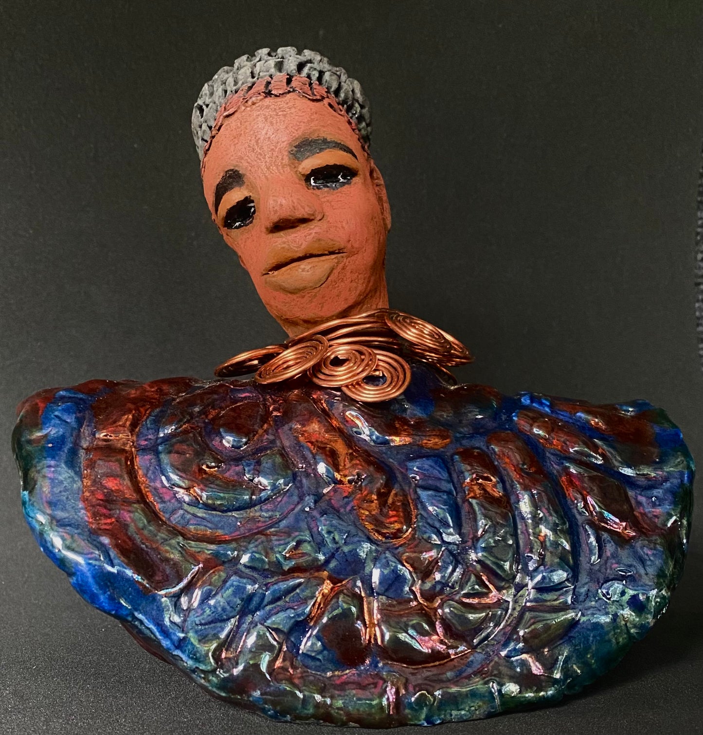 Meet Tia! Tia looks up with joy and anticipation! Tia stands 7" x 6" x 4" and weighs 1.90 lbs. She has a beautiful textured copper and blue robe. Tia has braided clay hair up in a bun. She has a honey brown complexion and soft light brown lips. Tia will make for great conversation in your home. Free Shipping! Check out our Shipping and Return policy