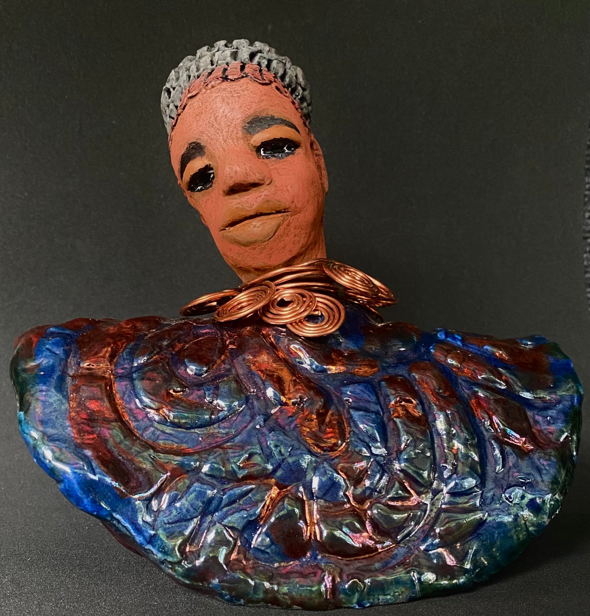 Meet Tia! Tia looks up with joy and anticipation! Tia stands 7" x 6" x 4" and weighs 1.90 lbs. She has a beautiful textured copper and blue robe. Tia has braided clay hair up in a bun. She has a honey brown complexion and soft light brown lips. Tia will make for great conversation in your home.  Free Shipping! Check out our Shipping and Return policy
