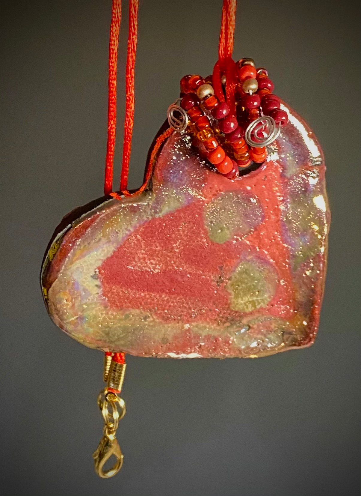 Have A Heart ! Each heart pendant is handmade with love! It is 3"x 3" and weighs approx. 3ozs. This pendant has a red violet and gold metallic raku glazes that renders a unique translucent patina. The heart has a textured pattern . Both sides are are different and equally beautiful! It holds a spiral of red violet mini beads on a spiral copper wire. This pendant has a nice 12" red suede cord!