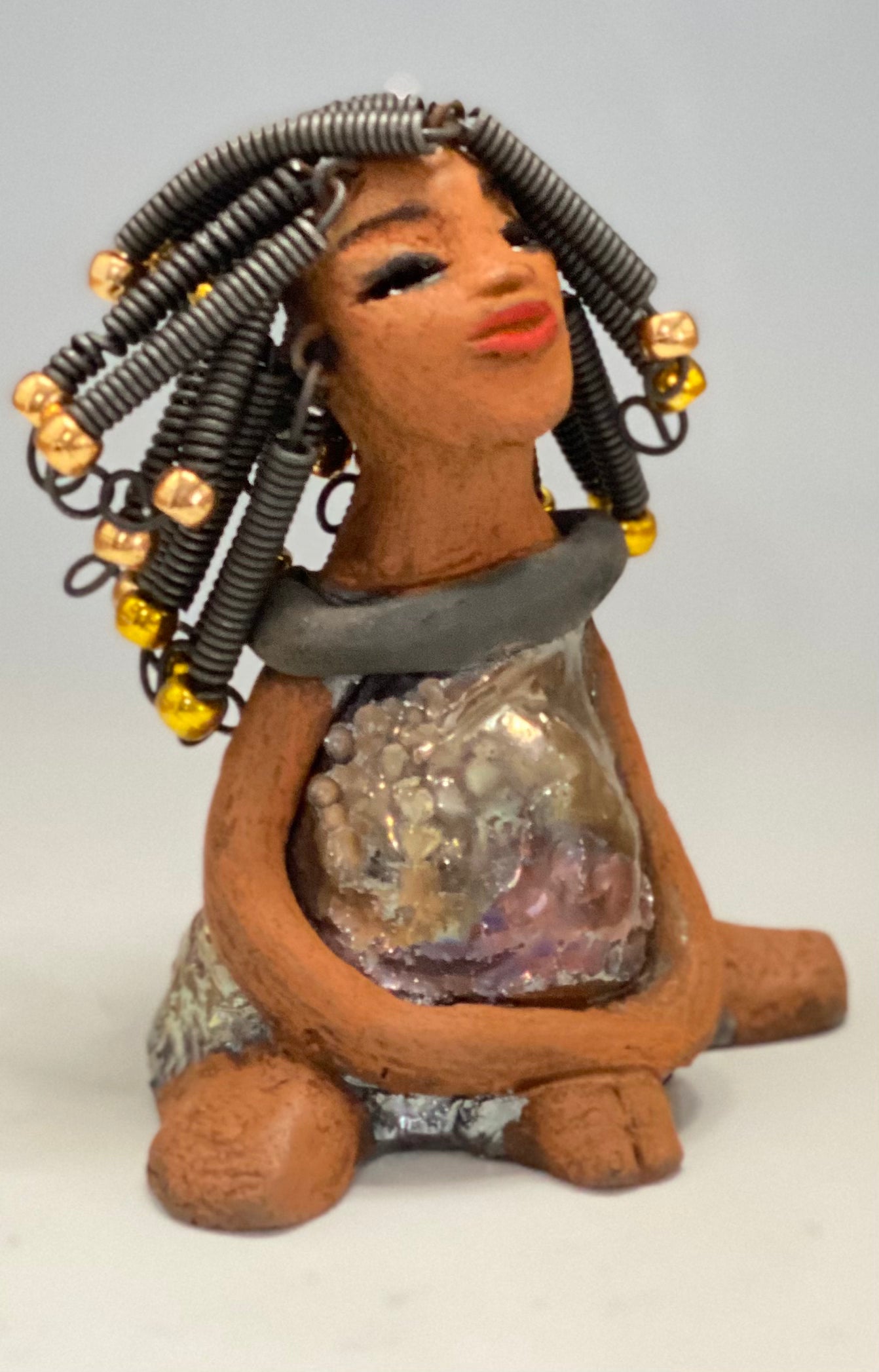 Meet Sadie Sadie stands 5.5" x 4" x 3" and weighs 8.7 ozs. She wears a lovely glossy metallic gold dress.. Sadie has over15 feet of coiled wire hair. Sadie appears to sit in a yoga pose. Her long arms rest at her side. Sadie is a great starter piece from the Herdew Collection!