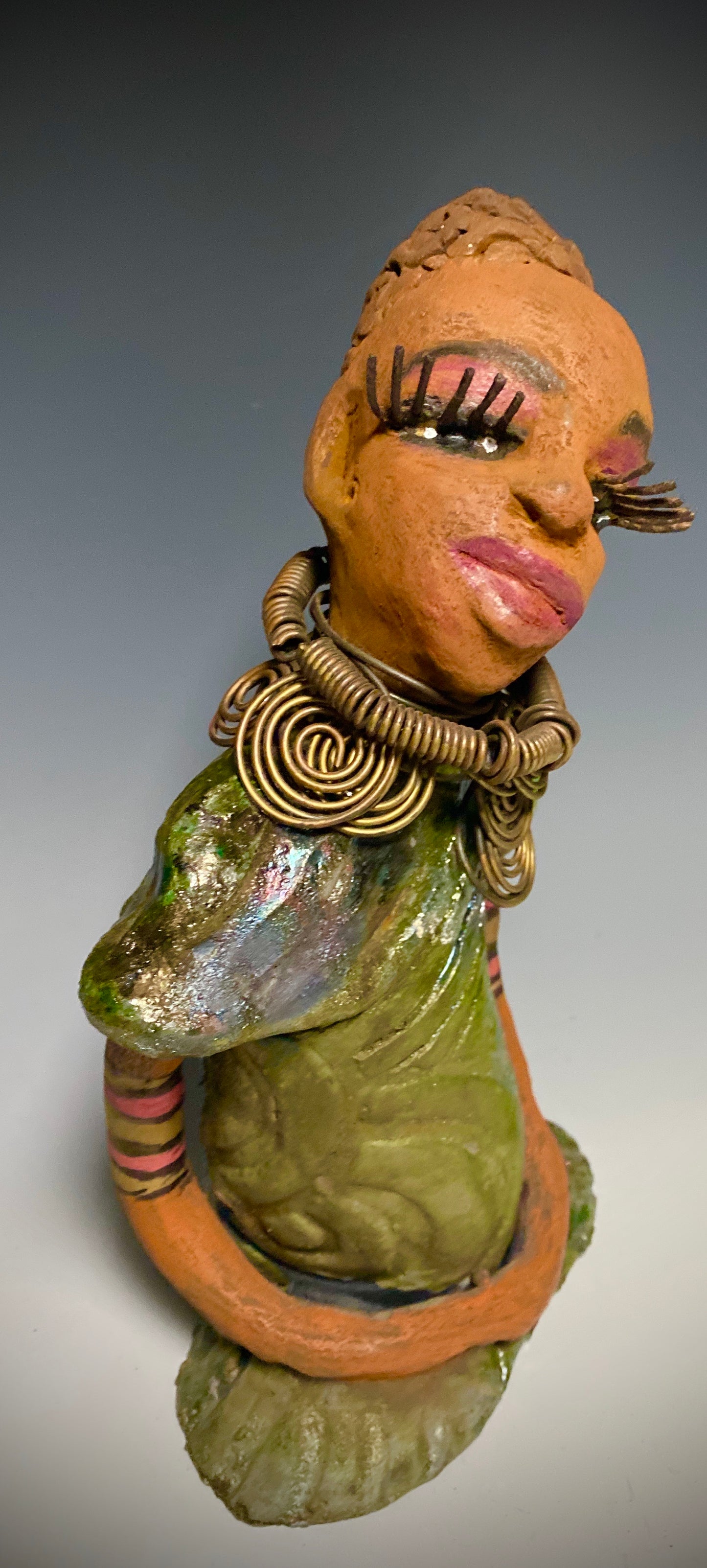Meet Sonya! Sonya stands 10" x 6" x 4" and weighs 2.3 lbs. She has a lovely honey brown complexion with reddish brown lips. She has a braided hairstyle. Sonya has a colorful metallic green antique copper glazed dress. She wears an awesome antique gold spiral necklace. Her long loving arms rest at her side. With long lashes and eyes wide opened, Sonya has hopes of finding a new home. Sonya will attract and spark conversation with guest in your home!