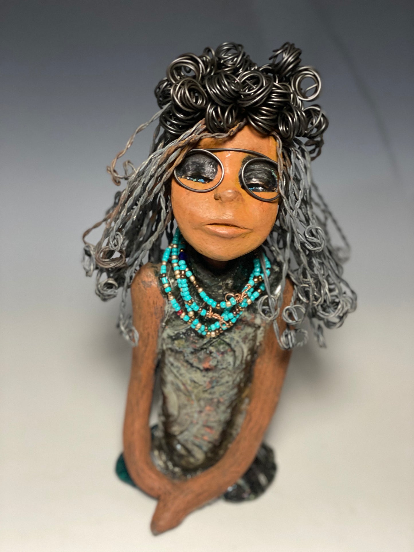 Meet Clarice! Clarice stand 13" x 6" x 5" and weighs 4.03 lbs. She has a lovely honey brown complexion with big bright eyes. Clarice wears glasses now! Her Herdew took over 2 hours to complete. It's made with 16 gauge wire. Clarice's dress is alligator green with streaks of copper. She has a blue beaded spiral necklace around her neck. Clarice looks to have a New ExtrArtindary Vision for 2021!