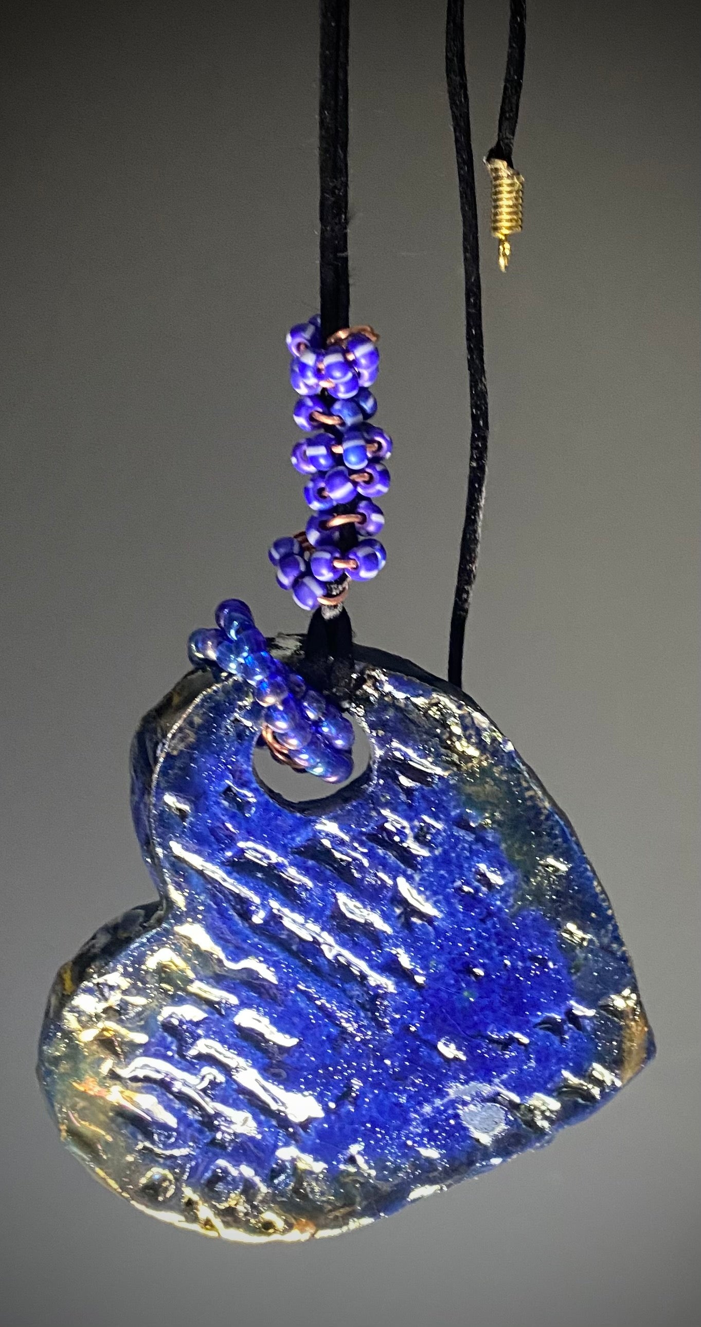 Have A Heart! Each heart pendant is handmade with love! It is 3"x 3"and weighs approx. 3ozs. This pendant has a blue and gold raku glazes that renders a unique translucent patina. The heart has a textured pattern! Both sides are are different and equally beautiful! There is a spiral of blue mini beads on copper in the center. This pendant has a nice 12" black adjustable rattail cord!