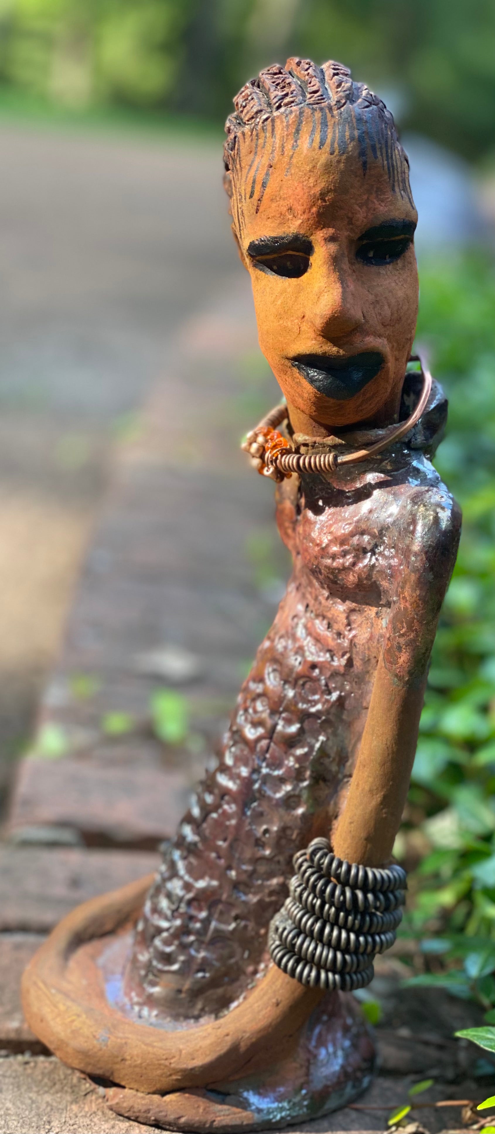 Jessie says no to wire hair and yes to the braids. Jessie stands 12" x 5" x 4.5" and weighs 1.03 lbs. She has a lovely honey brown complexion.  Jessie long loving arms rest beside her alligator copper green dress. She wears a strand of amber beads with spiral copper that can be worn as a bracelet. Jessie is a sophisticated lady that will grace your home.