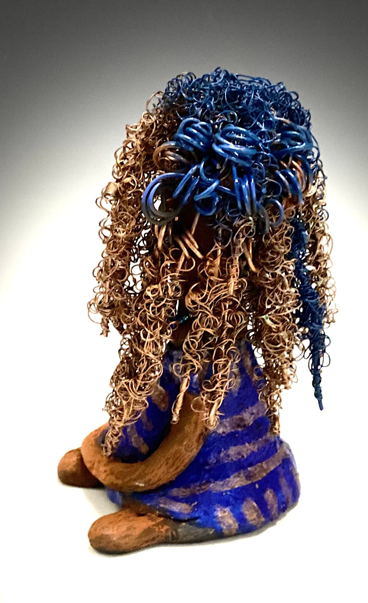 Sherrie stands 6" x 4" x 4.5" and weighs 12.6 ozs. She has a lovely honey brown complexion with reddish brown lips. Sherrie's hairstyle is made up of over 75 feet of twisted 24 gauge wire. Sherrie has a striped metallic copper and blue glazed dress. She wears a aqua blue beaded necklaces. With eyes wide opened, Sherrie has hope of finding a new home. She will make an excellent starter piece from the HerDew collection!