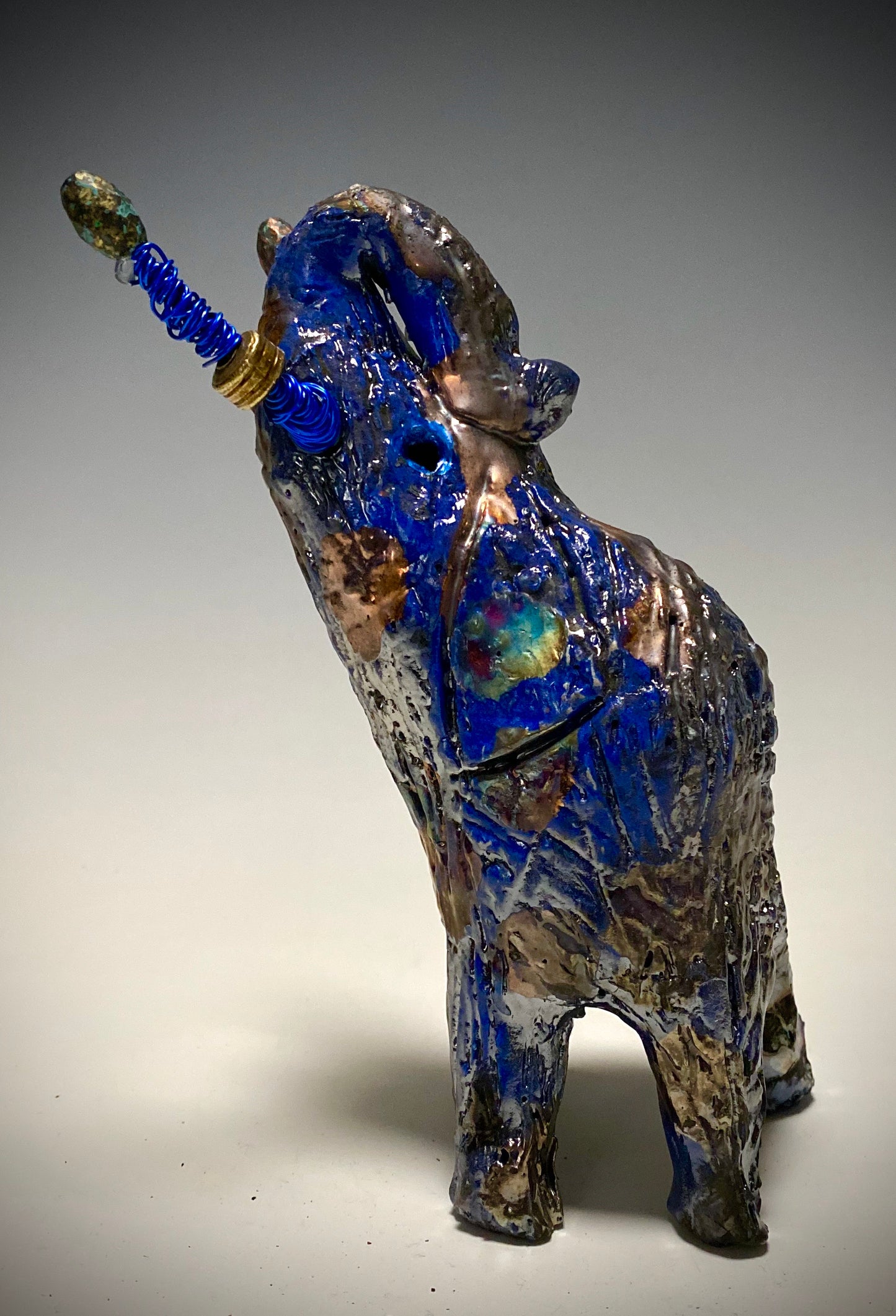 Raku Elephant Have you HERD!!!!!! Just one of these lovely Raku Fired Elephant will make an excellent gift for your friend, sorority or for your home’ special place centerpiece. 7" x 4" x 4" 14 ozs. Blue wire beaded blue tusk Beautiful metallic raku colors For decorative purposely only.