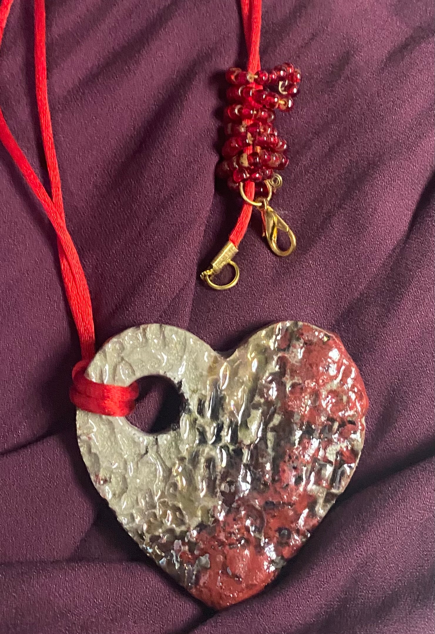 Have A Heart ! Each heart pendant is handmade with love! It is 3"x 3" and weighs approx. 3ozs. This pendant has a copper gold metallic raku glazes that renders a unique translucent  patina. The heart has a textured pattern . It holds a spiral of red mini beads on a spiral copper wire. This pendant has a nice 12" red suede cord!