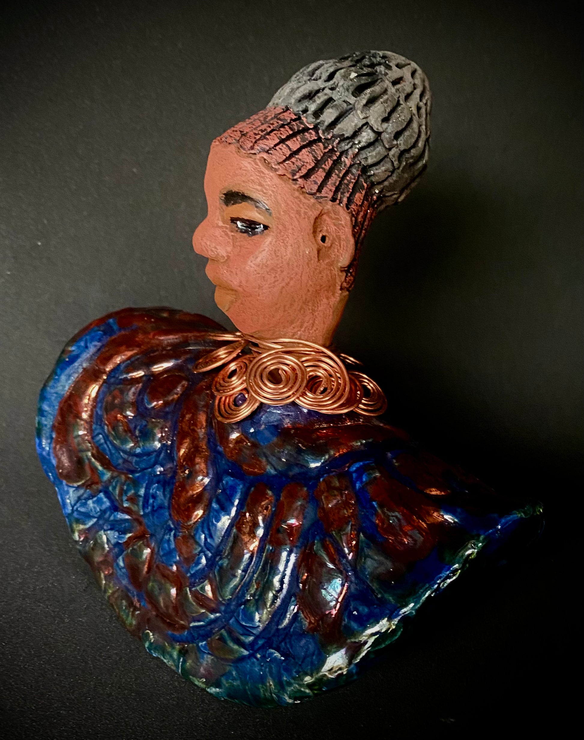 Meet Tia! Tia looks up with joy and anticipation! Tia stands 7" x 6" x 4" and weighs 1.90 lbs. She has a beautiful textured copper and blue robe. Tia has braided clay hair up in a bun. She has a honey brown complexion and soft light brown lips. Tia will make for great conversation in your home.  Free Shipping! Check out our Shipping and Return policy