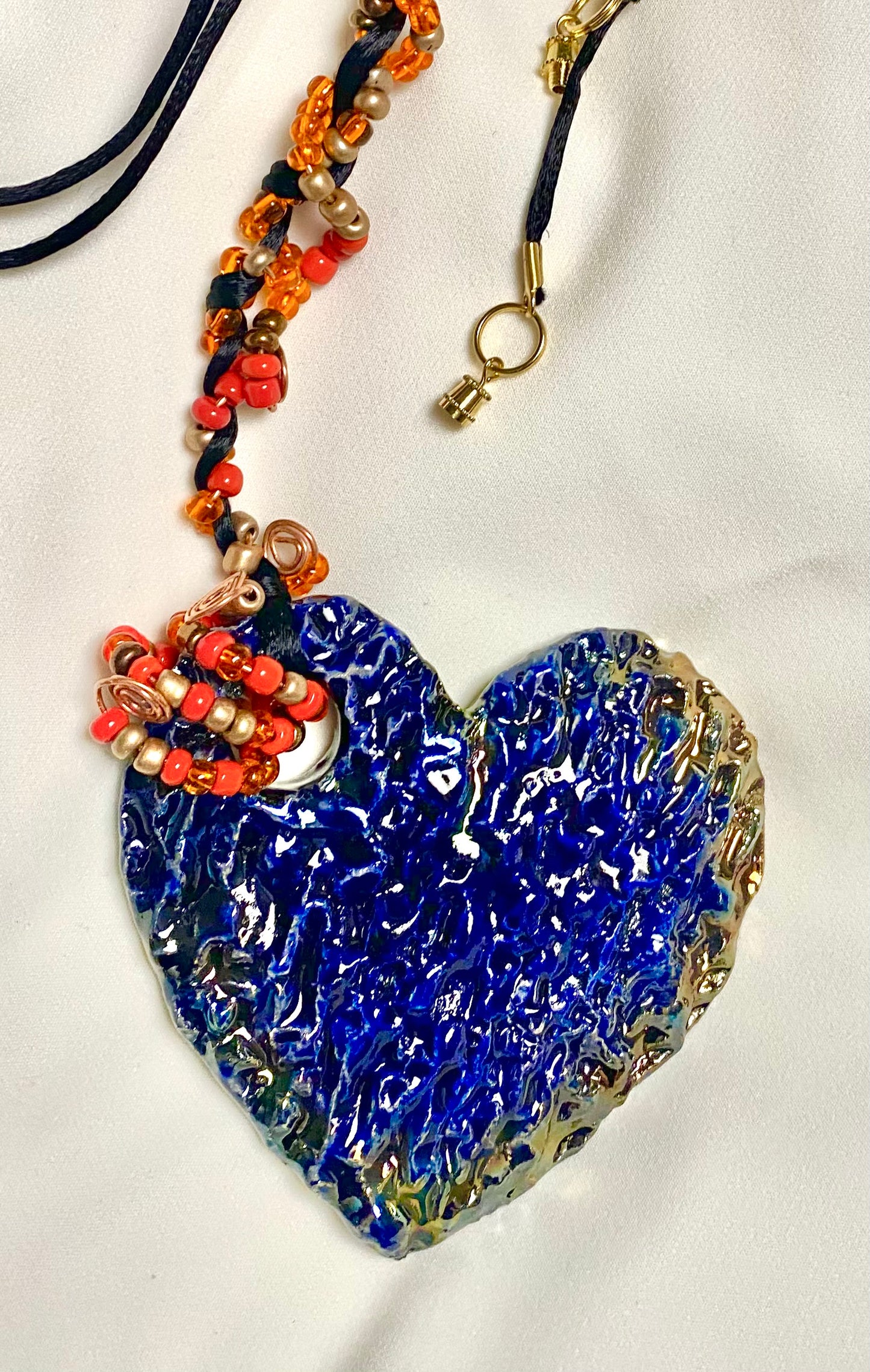 Have A Heart ! Each heart pendant is handmade with love! It is 3"x 3" and weighs approx. 3ozs. This pendant has a blue and gold metallic raku glazes that renders a unique translucent patina. The heart has a textured pattern . It holds a spiral of orange and red mini beads on a spiral copper wire. This pendant has a nice 12" black suede cord!