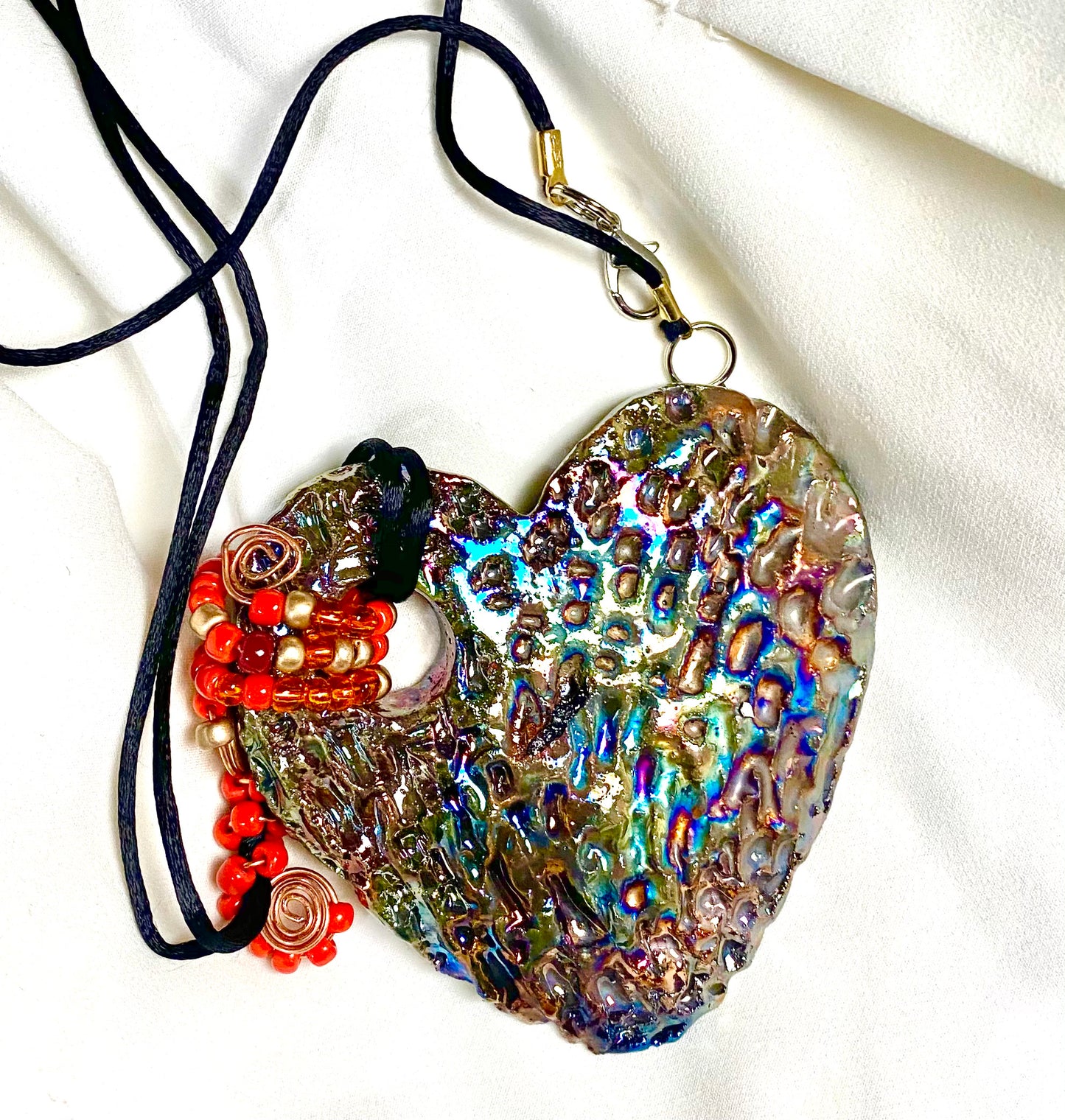 Have A Heart ! Each heart pendant is handmade with love! It is 3"x 3" and weighs approx. 3ozs. This pendant has a copper gold metallic raku glazes that renders a unique translucent patina. The heart has a textured pattern . It holds a spiral of amber and red mini beads on a spiral copper wire. This pendant has a nice 12" black suede cord!