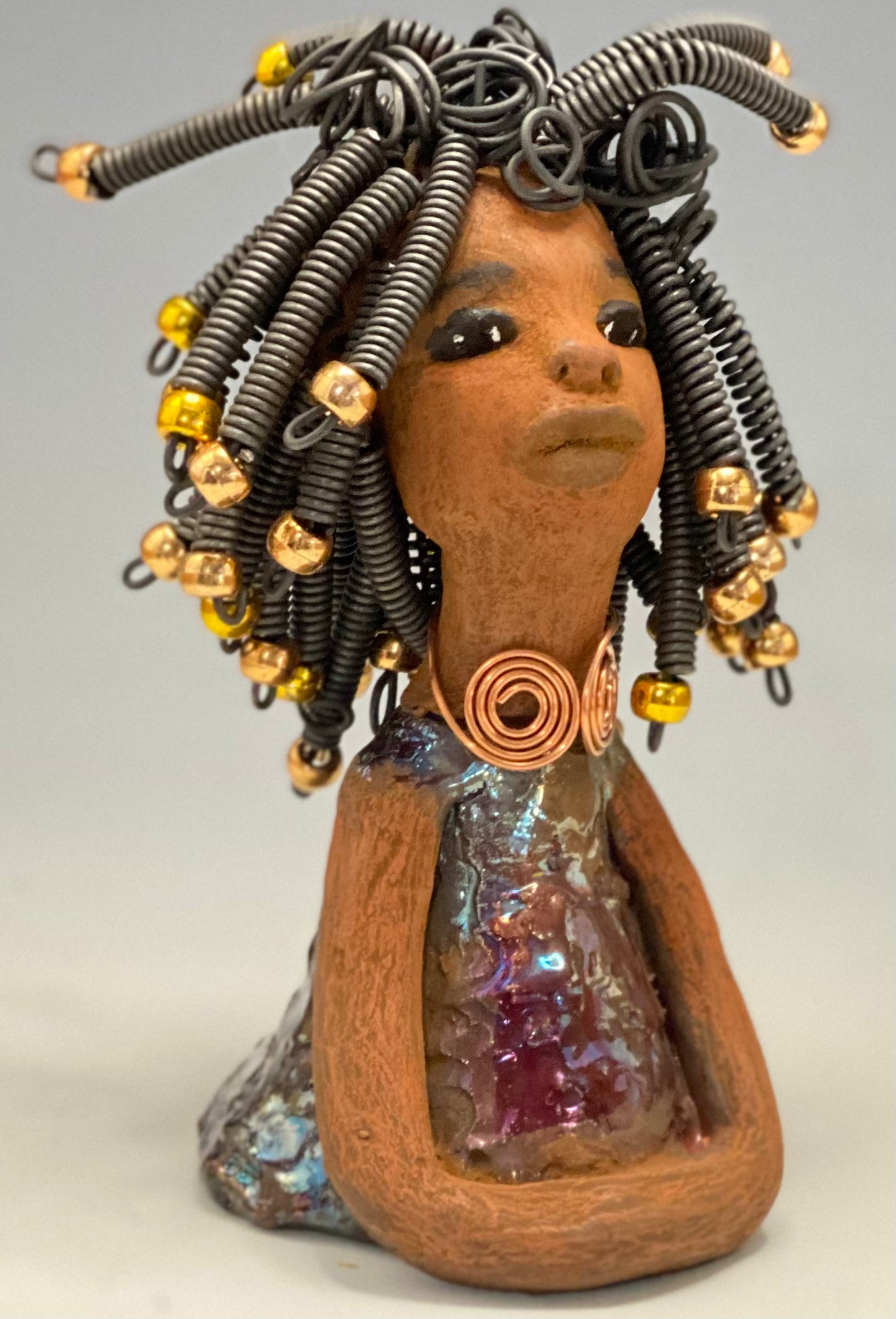 Meet Alexus Alexus stands 7.5" x 4" x 4" and weighs 1.05 lbs. She wears a lovely glossy metallic gold dress adorn by a spiral copper necklace. Alexus has over15 feet of coiled wire hair with gold beads.. Alexus appears to sit in a yoga pose. Her long arms rest at her side. Alexus is a great starter piece from the Herdew Collection!