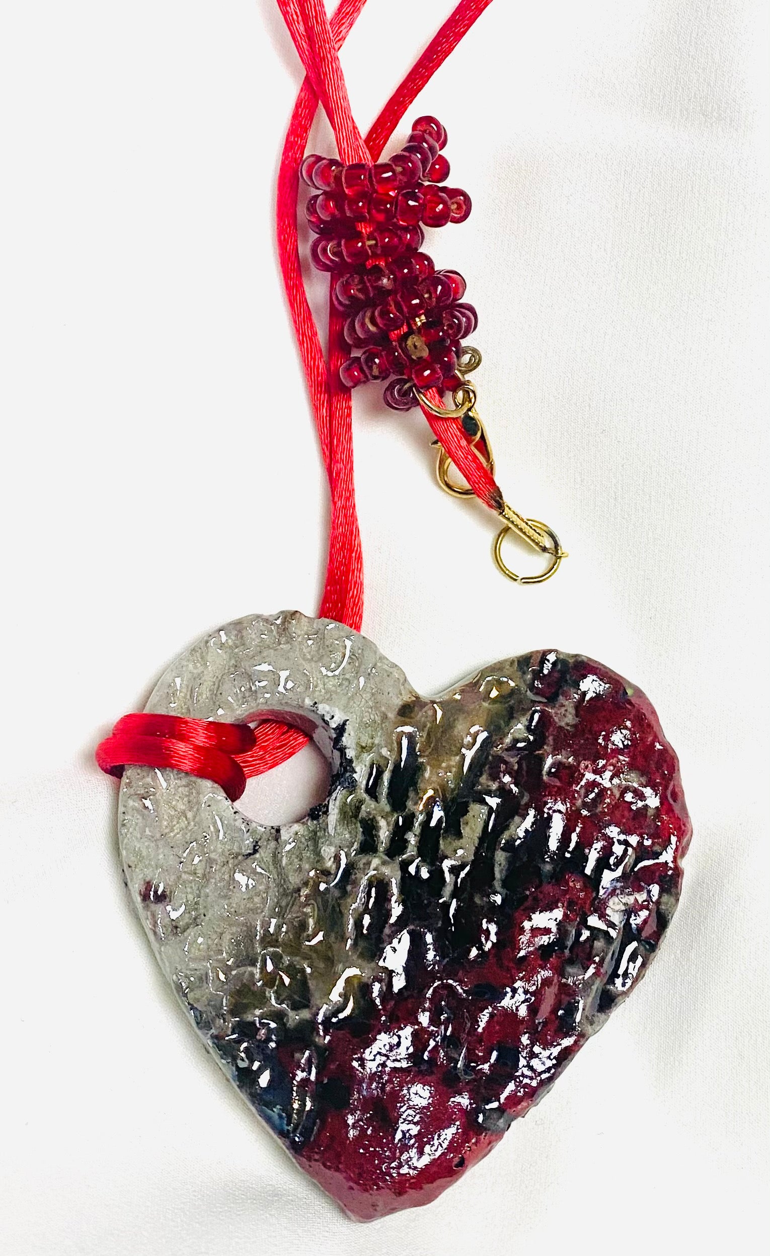 Have A Heart ! Each heart pendant is handmade with love! It is 3"x 3" and weighs approx. 3ozs. This pendant has a copper gold metallic raku glazes that renders a unique translucent  patina. The heart has a textured pattern . It holds a spiral of red mini beads on a spiral copper wire. This pendant has a nice 12" red suede cord!